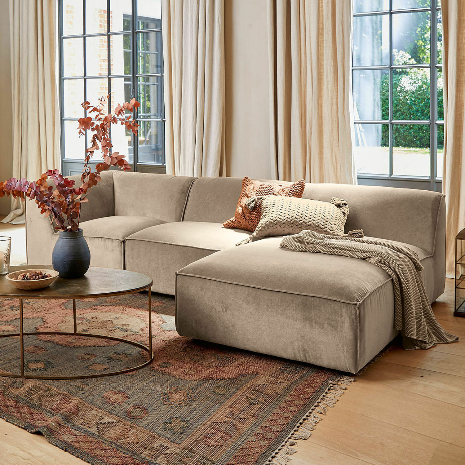 Sofa McLean Beżowa sofa narożna z miękkiego materiału w stylowym salonie z dywanem i stolikiem kawowym