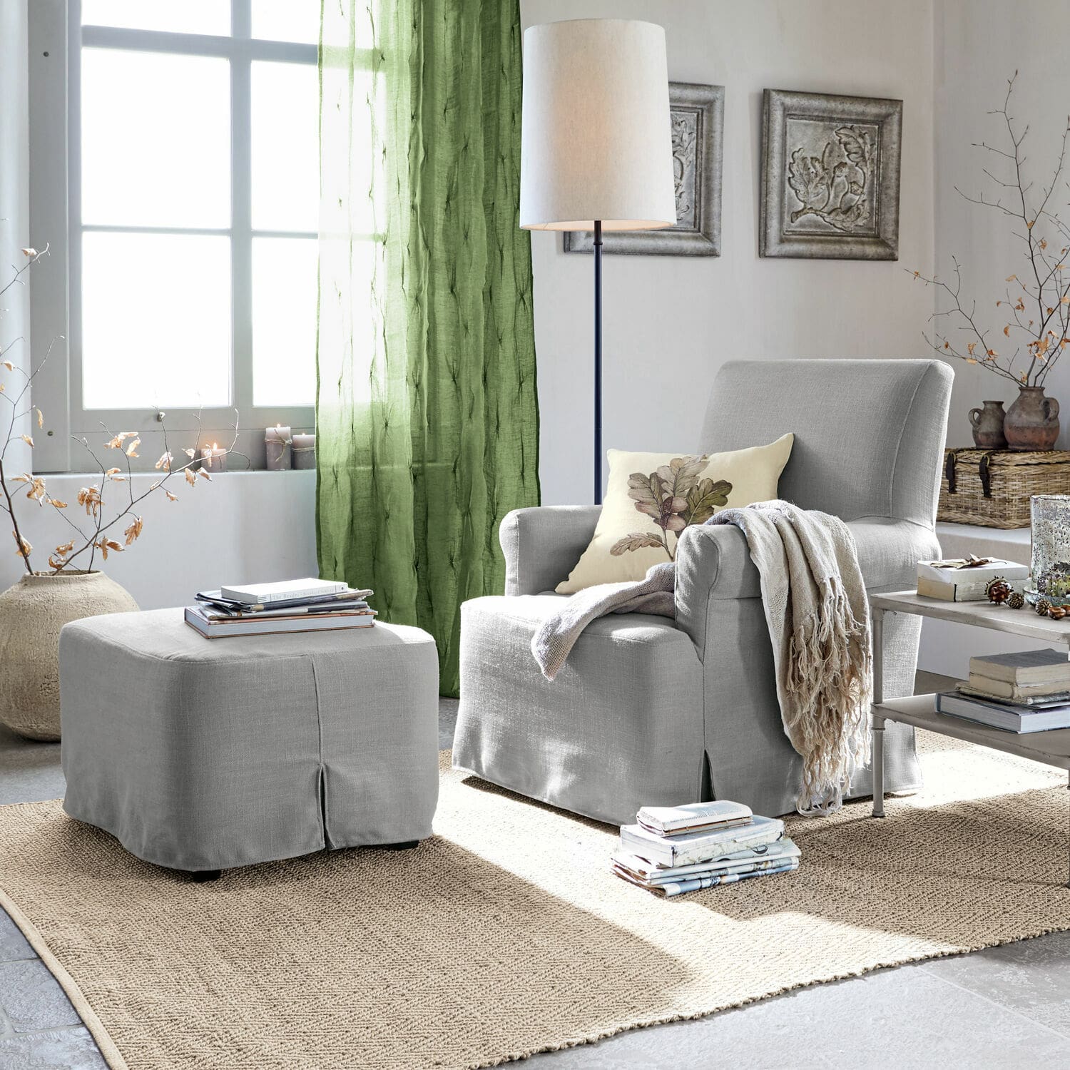 Fotel z podnóżkiem Nasour Szara tapicerowana sofa z podnóżkiem i zielonymi zasłonami w jasnym salonie z dywanem z juty