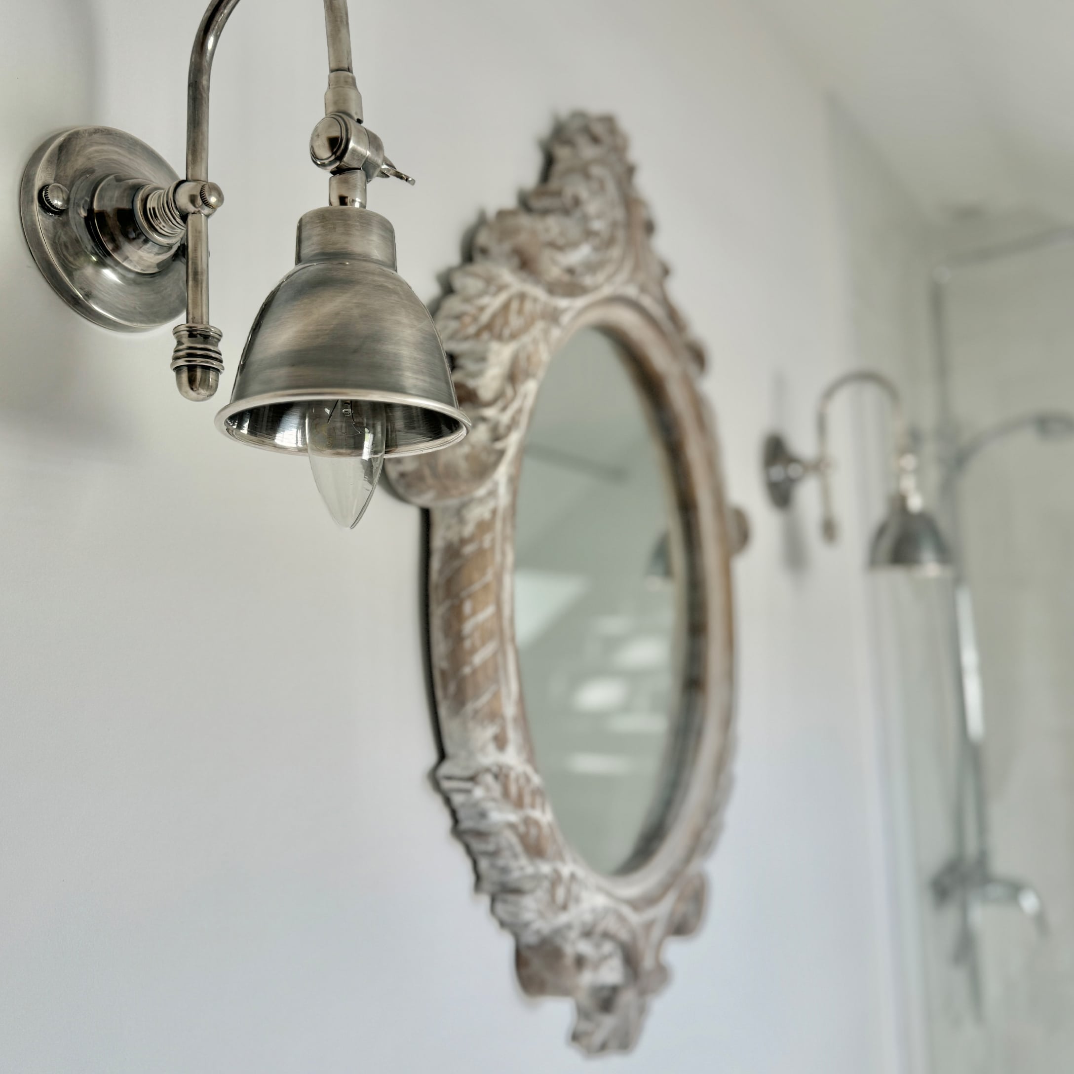 Metalowa lampa ścienna w stylu vintage obok ozdobnego lustra w łazience