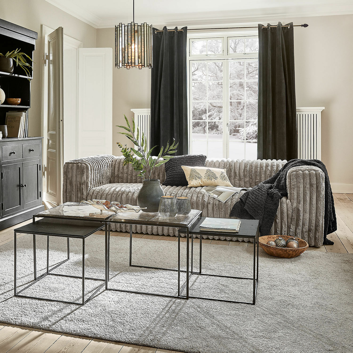Sofa Roucemont Nowoczesny salon z szarą, miękką kanapą i zestawem metalowych stolików kawowych na jasnym dywanie