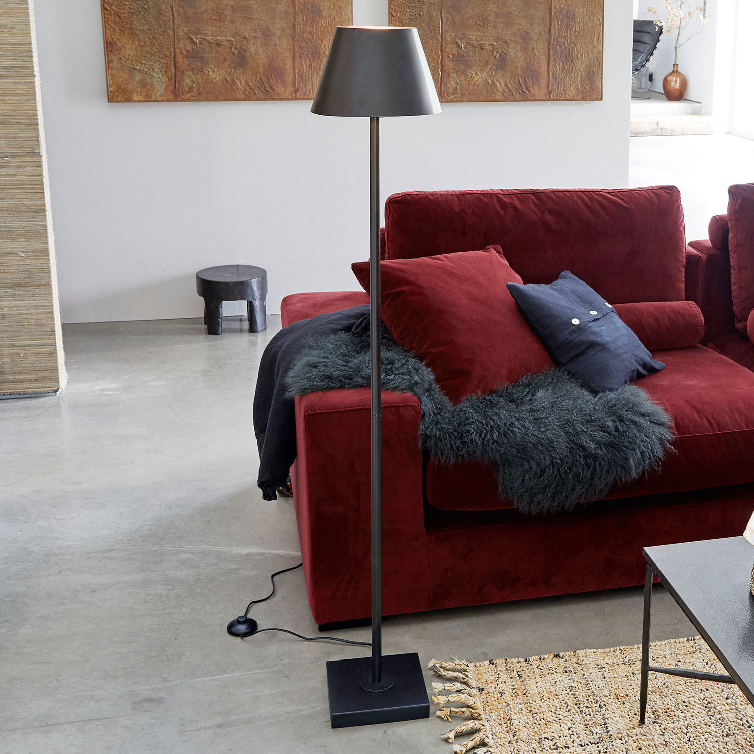 Lampa stojąca Marjan Czarna metalowa lampa stojąca z kloszem obok czerwonej sofy i dywanu w nowoczesnym salonie