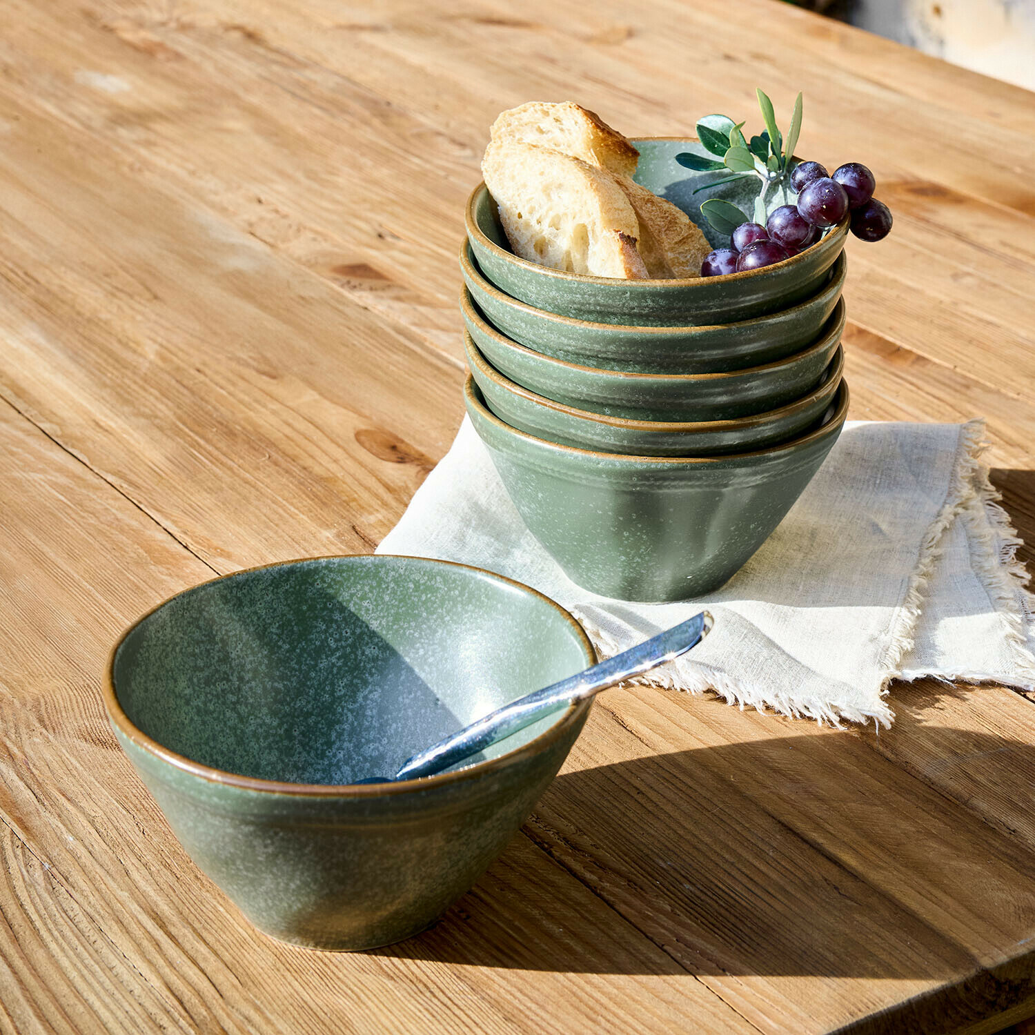 Zestaw zielonych ceramicznych misek na drewnianym stole z kromkami chleba i winogronami