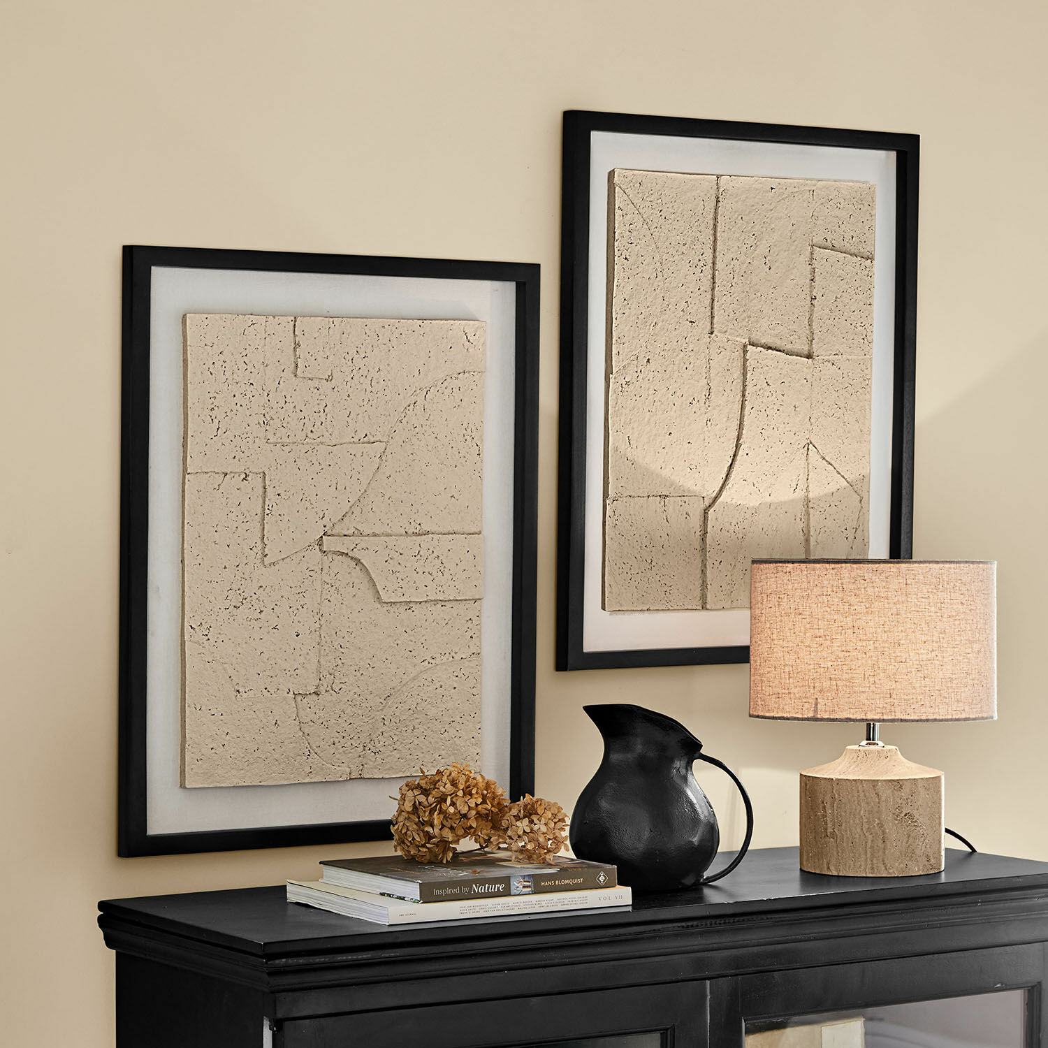 Obrazek, zestaw 2 szt. Lavinois Dwa beżowe reliefowe obrazy w czarnych ramach nad czarną komodą z lampą i czarnym dzbankiem