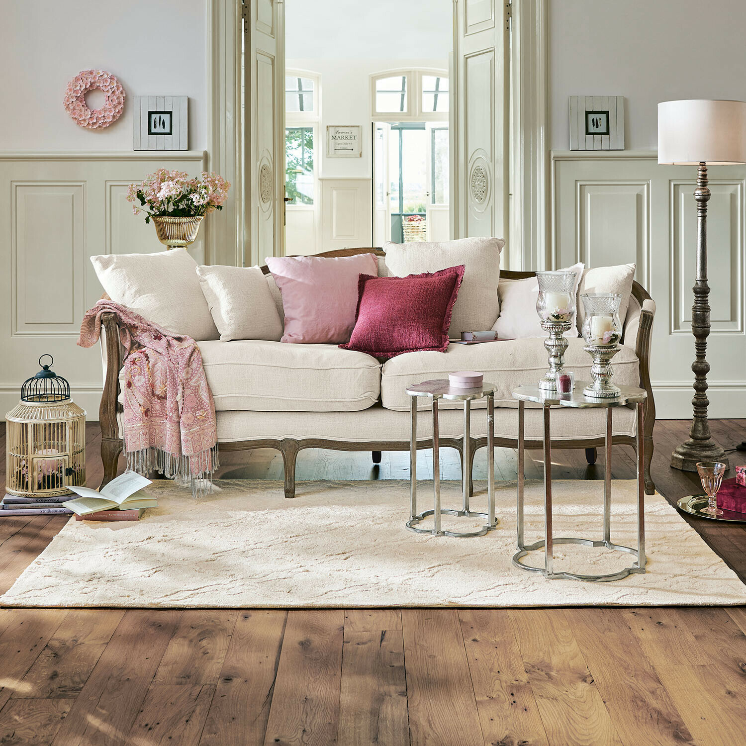 Sofa Monneville Beżowa sofa z drewnianą ramą i różowymi poduszkami w eleganckim salonie z dywanem i stolikami
