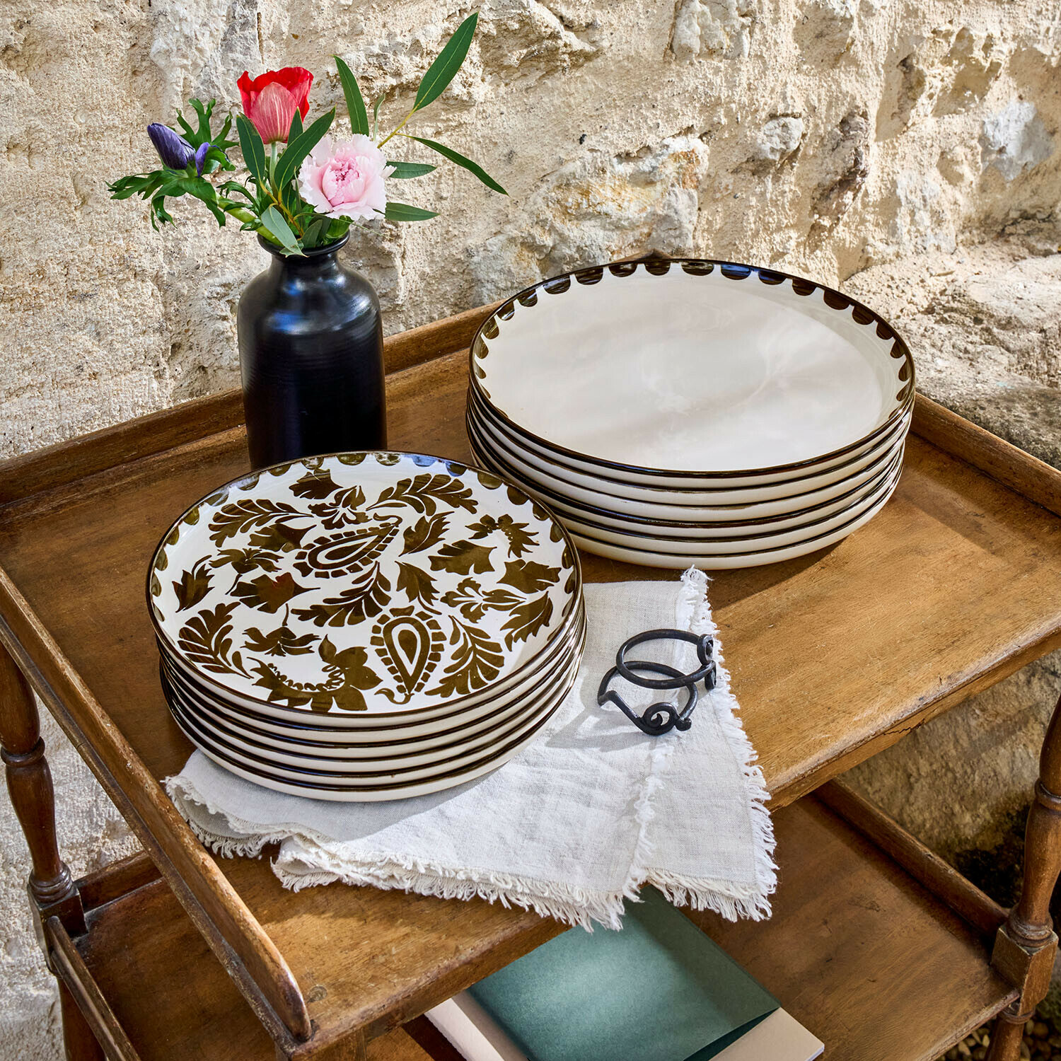 Talerz, zestaw 12 szt. Tazira Zestaw ceramicznych talerzy z brązowym wzorem i kremowym kolorem na drewnianym stoliku z czarnym wazonem i kwiatami