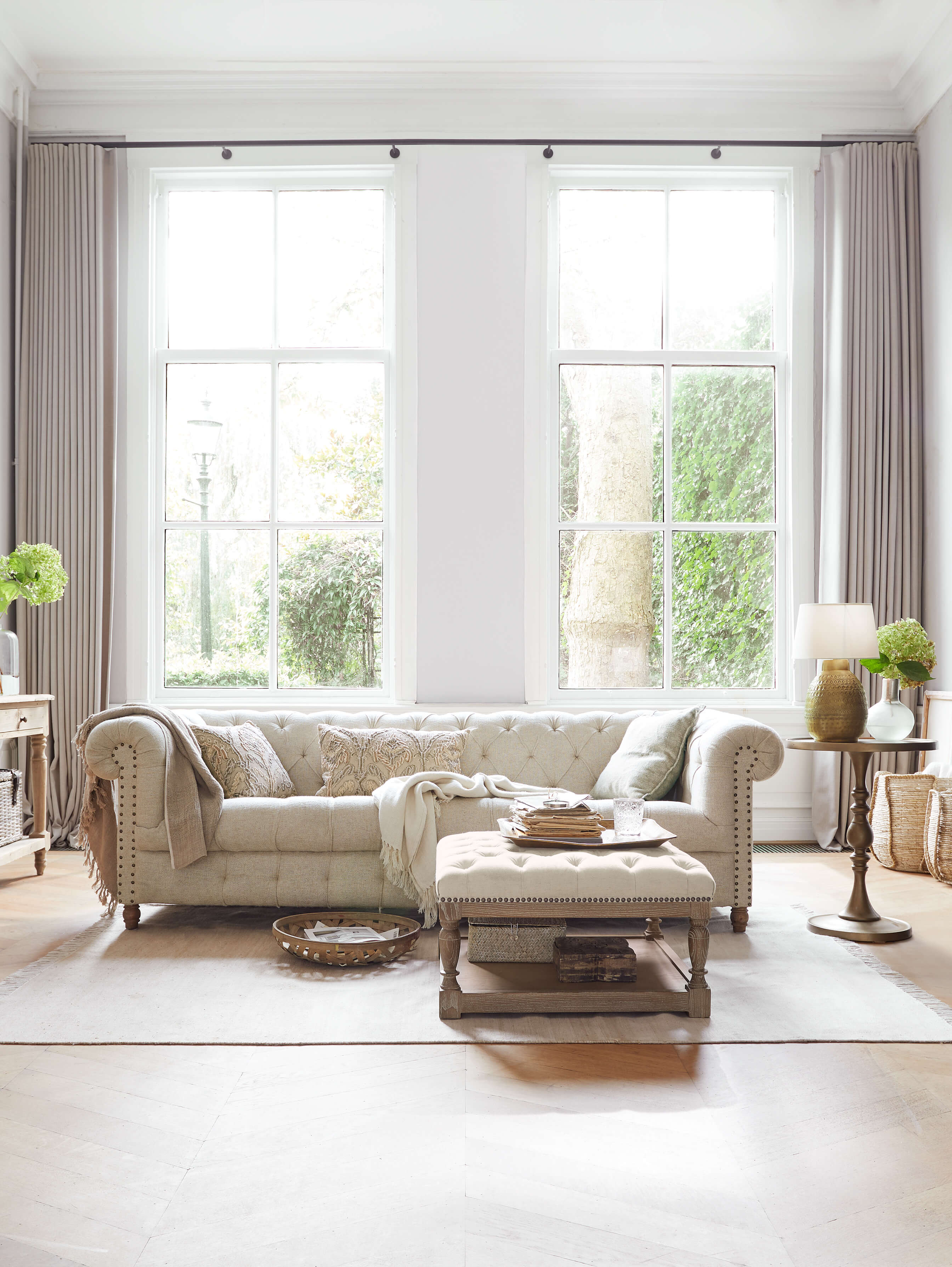 Beżowa pikowana sofa Chesterfield z tkaniny w jasnym salonie z naturalnym światłem