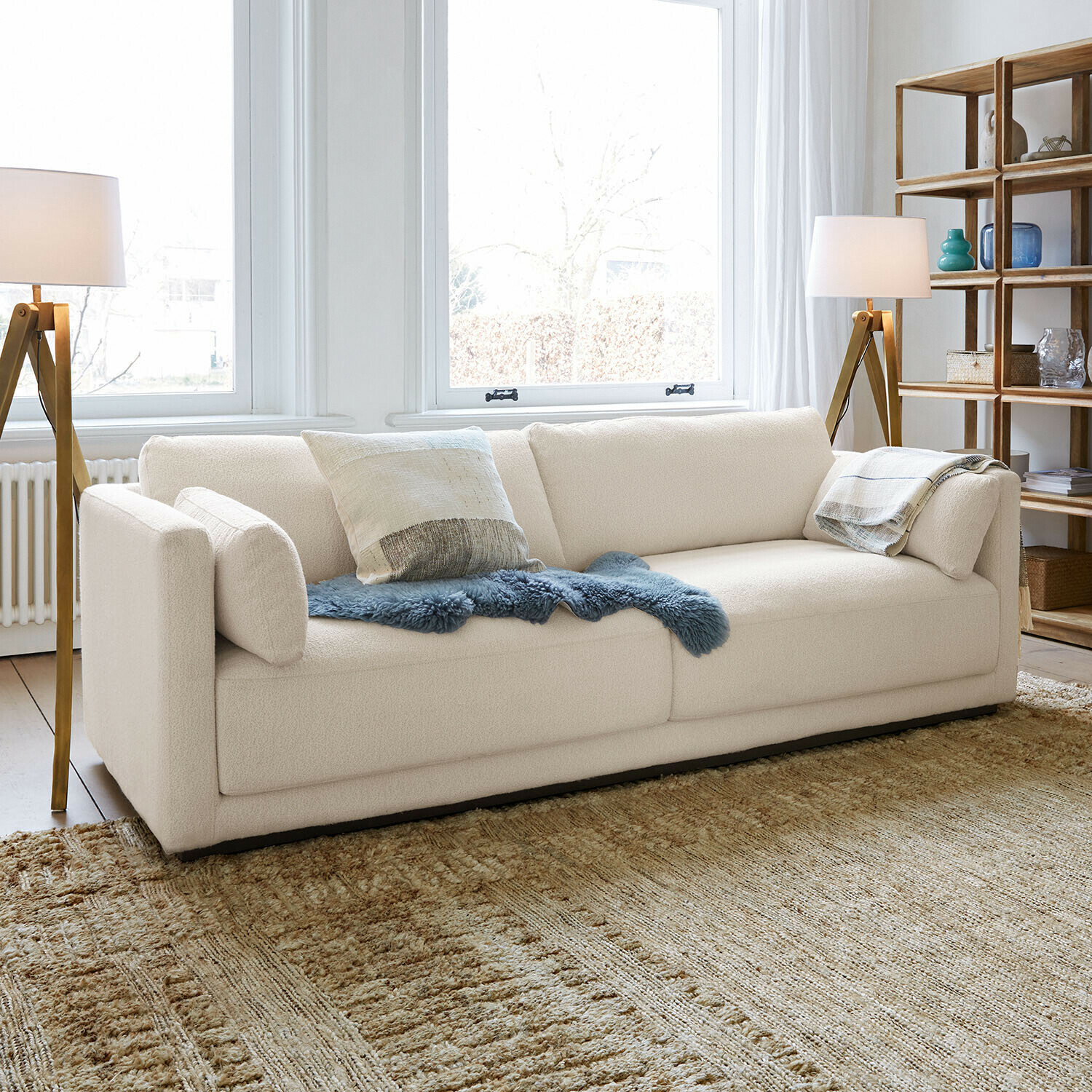 Sofa Thamira Nowoczesna kremowa sofa z miękką tkaniną i dekoracyjnymi poduszkami w jasnym salonie