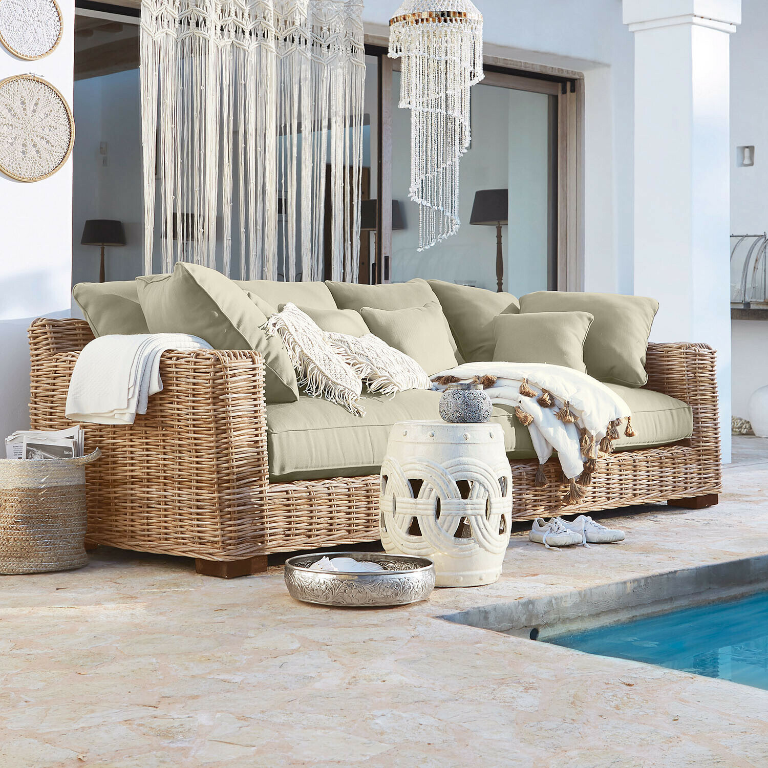 Sofa z rattanu z beżowymi poduszkami i dekoracjami w stylu boho przy basenie