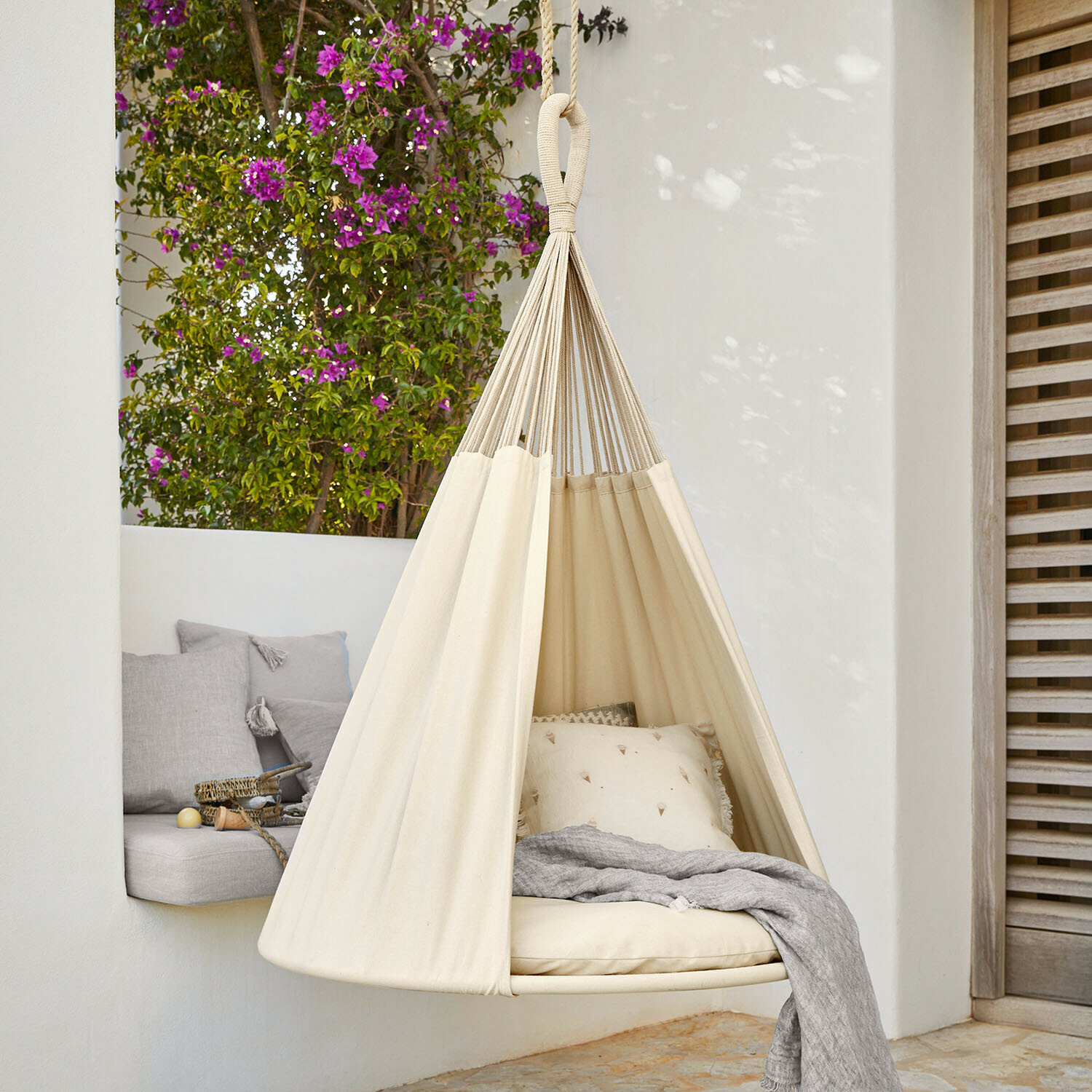 Beżowy hamak wiszący z bawełny z poduszkami i szarym kocem na tarasie z kwiatami