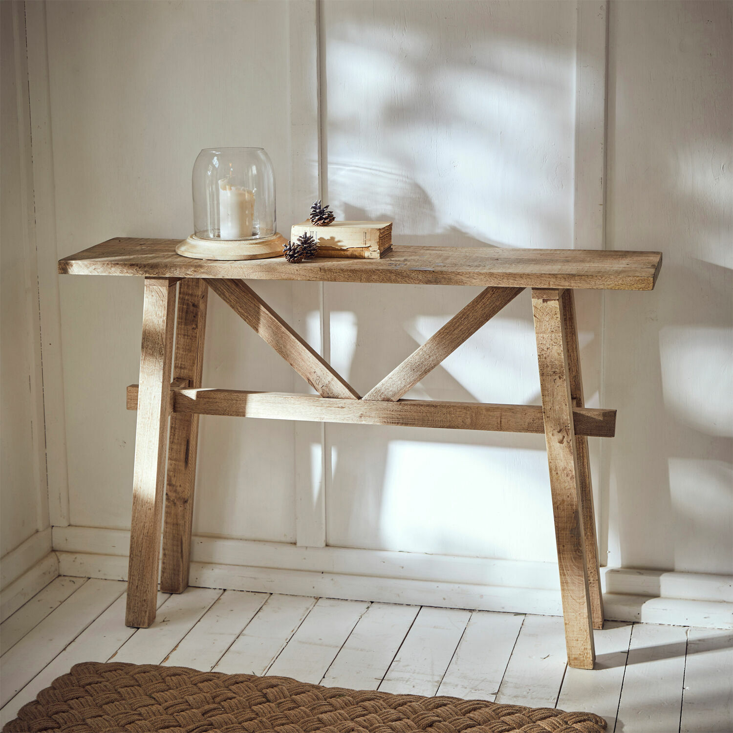 Konsola Nael Drewniany stół konsolowy w naturalnym kolorze z dekoracyjną świecą i książką na białej podłodze