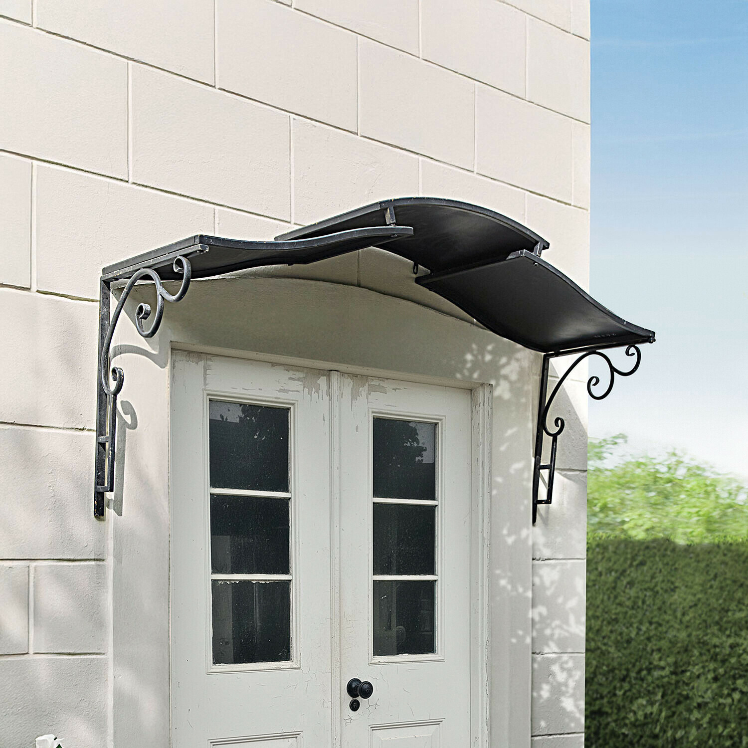 Czarny metalowy daszek nad białymi drzwiami z ozdobnymi wspornikami i falistym kształtem