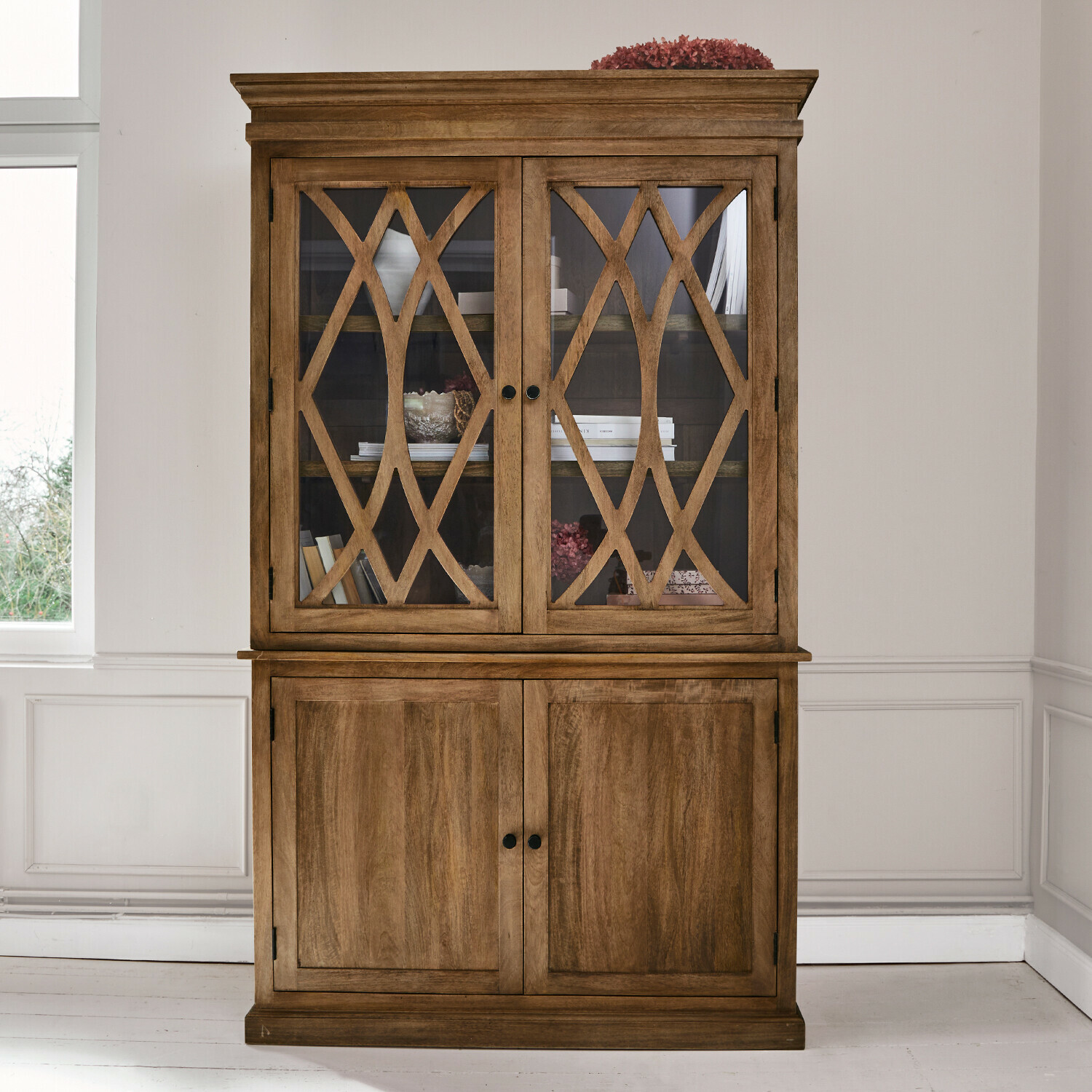 Drewniana witryna z ozdobnymi szklanymi drzwiami i dolną częścią z pełnego drewna w kolorze naturalnym