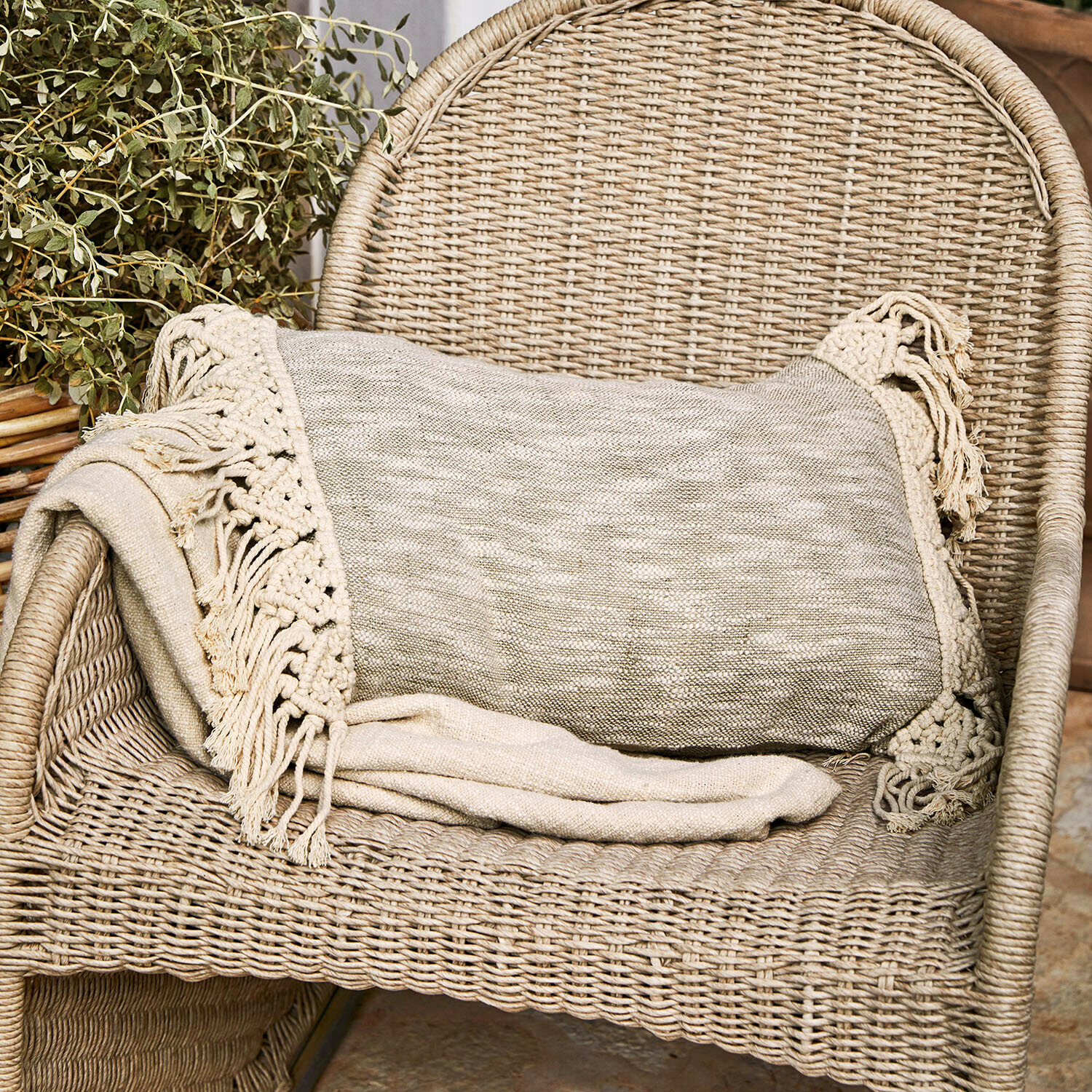 Beżowy pled z frędzlami na wiklinowym fotelu, dekoracja wnętrz i przytulny dodatek do salonu