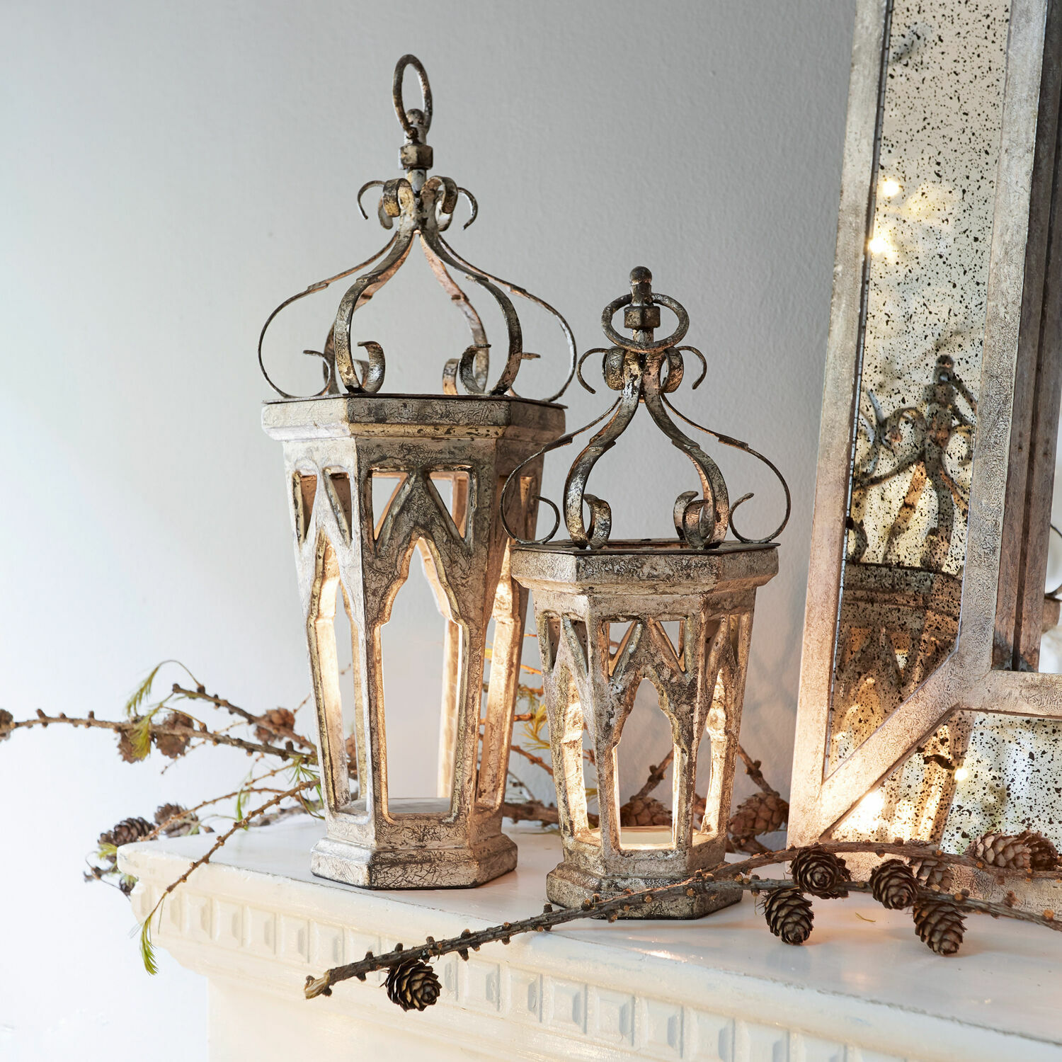 Dekoracyjne metalowe latarnie w stylu vintage w kolorze postarzanego srebra na kominku z szyszkami