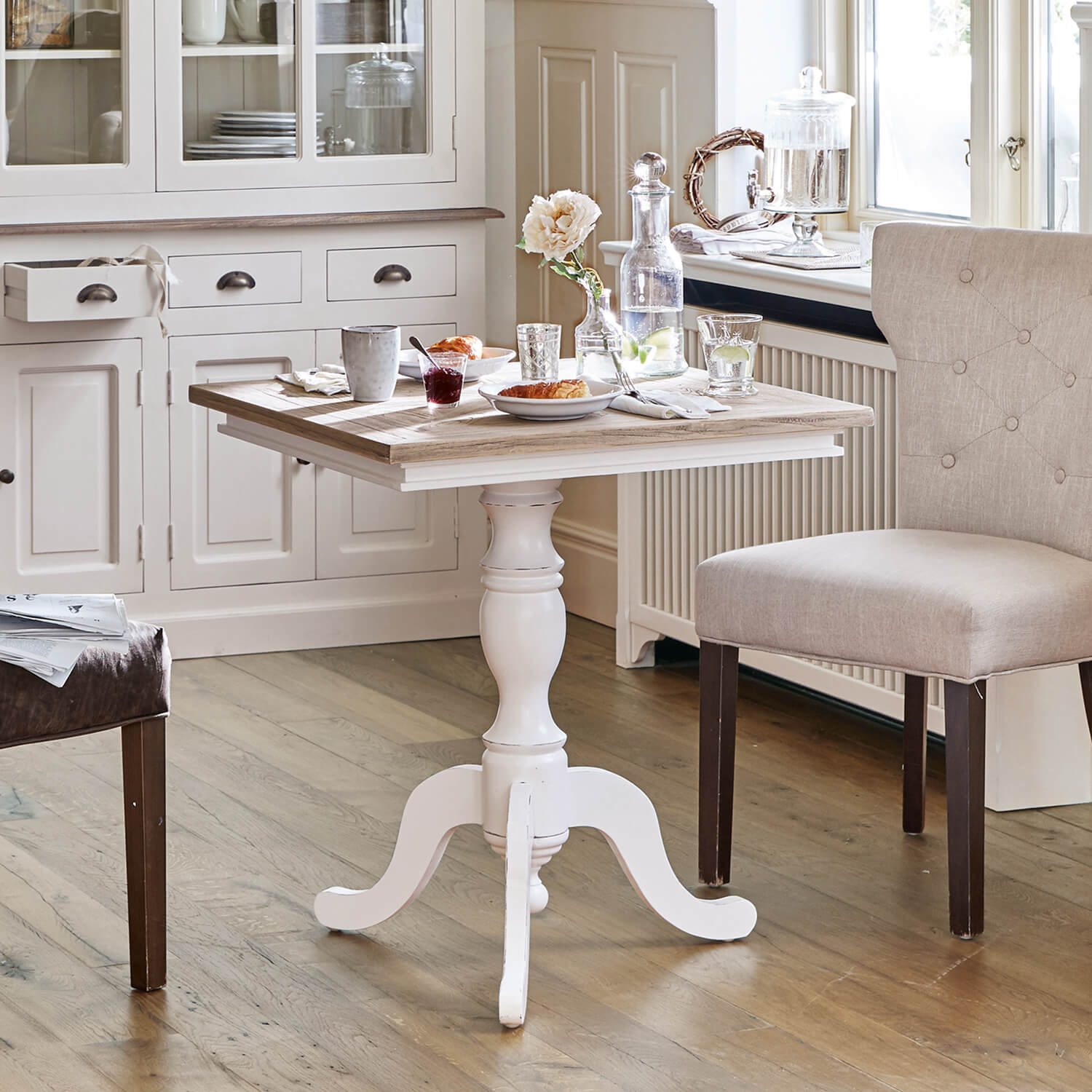 Biały drewniany stół z ozdobną nogą i jasnym blatem w przytulnej jadalni z krzesłami