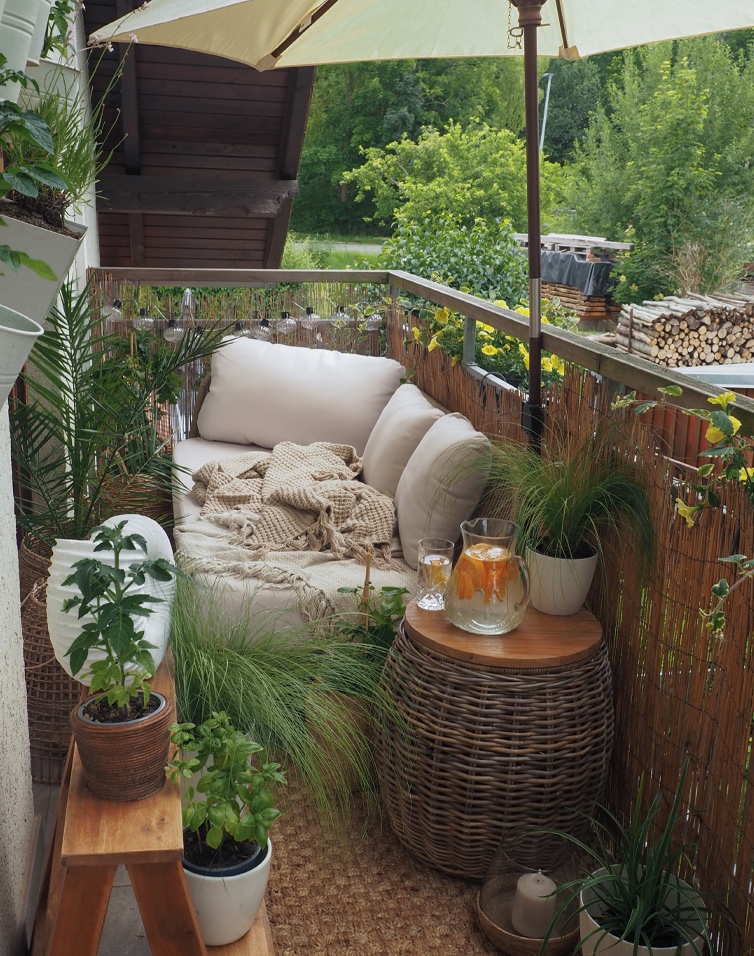 Przytulny balkon z beżową sofą z poduszkami i wiklinowym stolikiem, rośliny i parasol