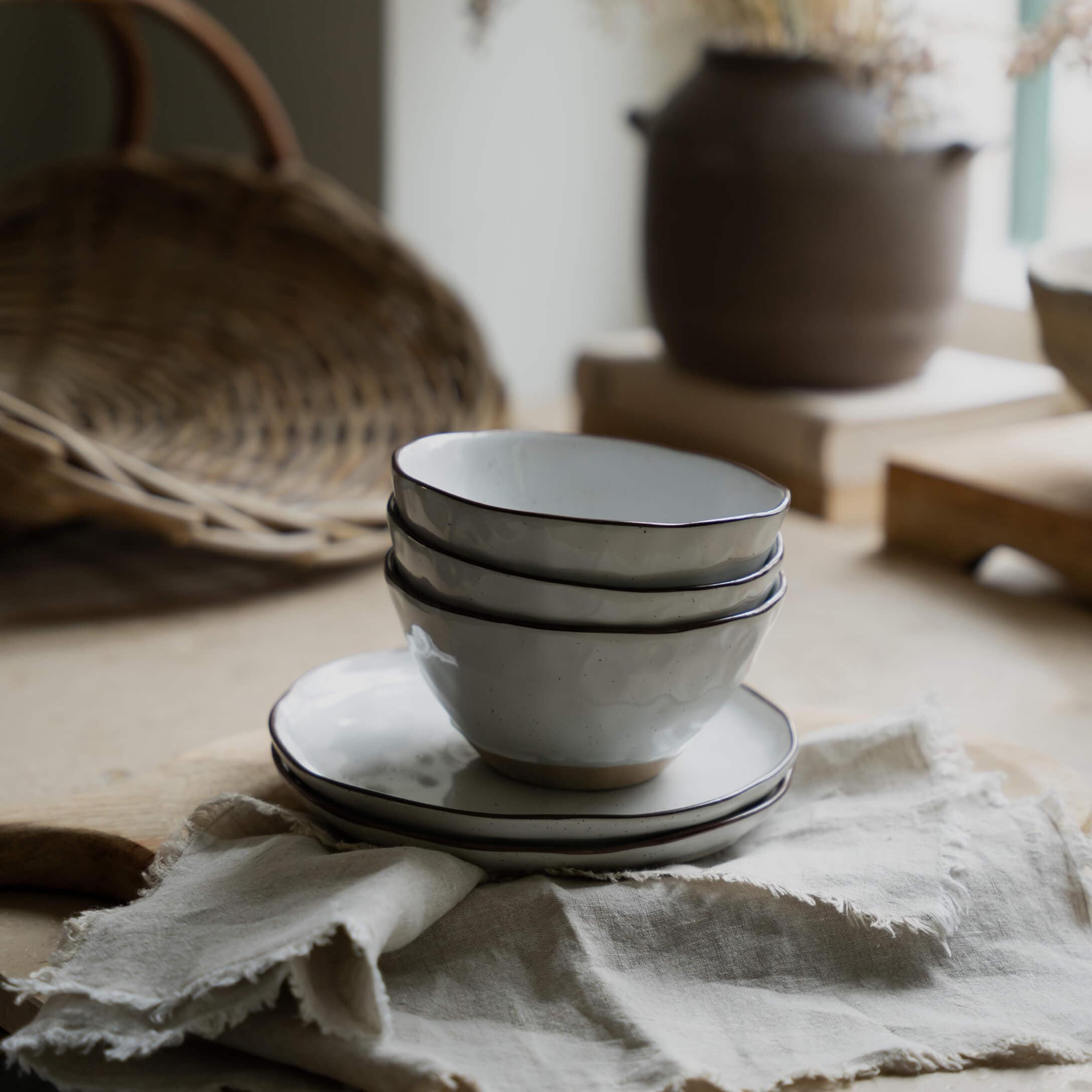 Zestaw białych ceramicznych misek i talerzy z czarną obwódką na lnianej tkaninie do kuchni