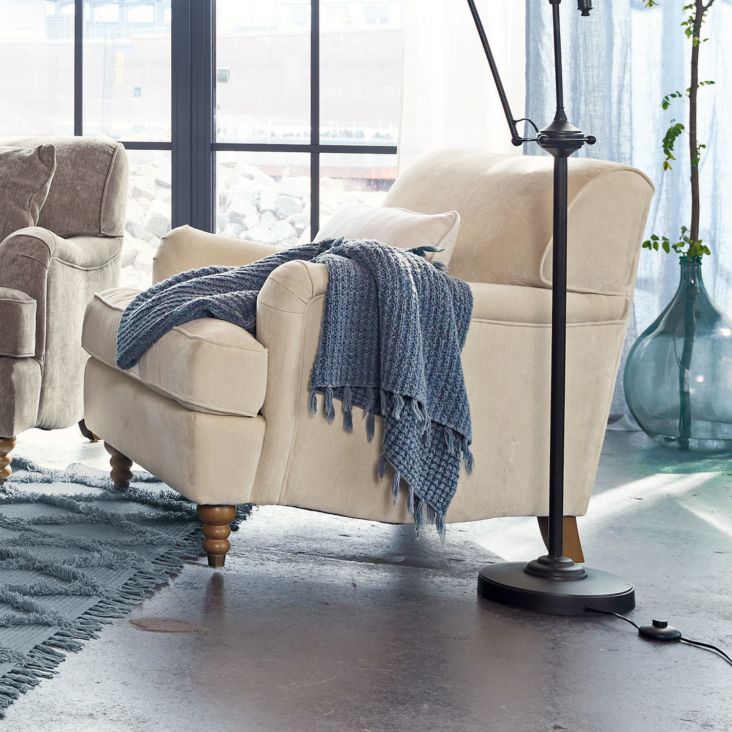 Fotel Isa Beżowa tapicerowana sofa z drewnianymi nogami i niebieskim dzianym kocem w nowoczesnym salonie