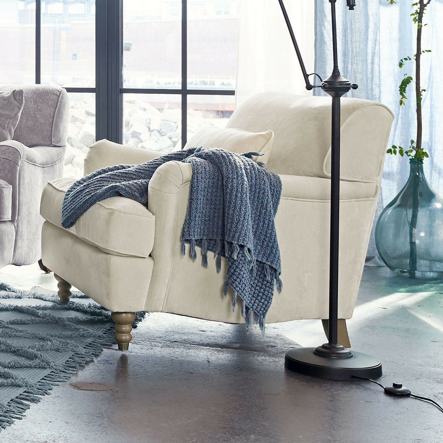 Fotel Isa Beżowa tapicerowana sofa z drewnianymi nogami i niebieskim dzianym kocem w nowoczesnym salonie