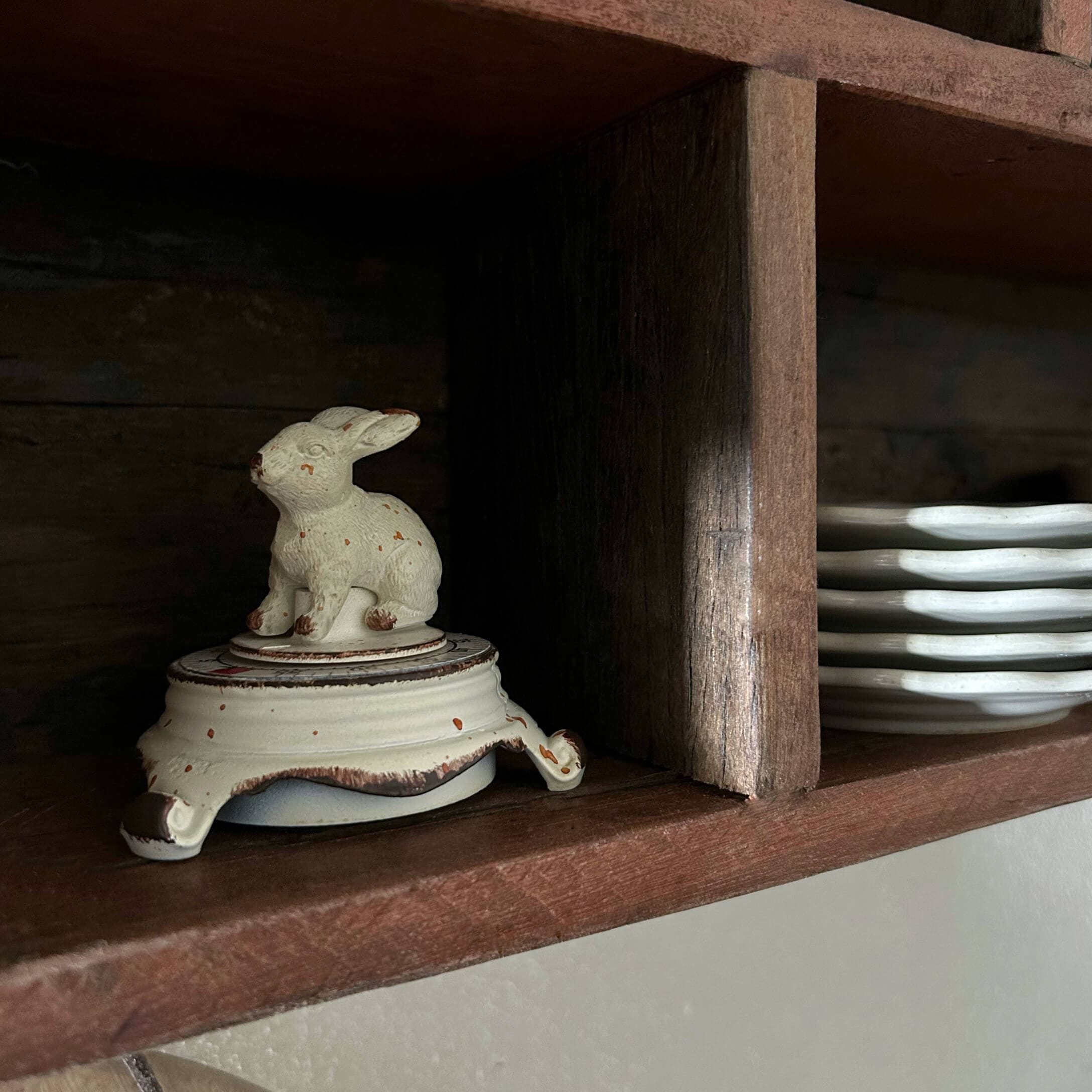 Biały ceramiczny pojemnik z pokrywką w kształcie królika na drewnianej półce z talerzami
