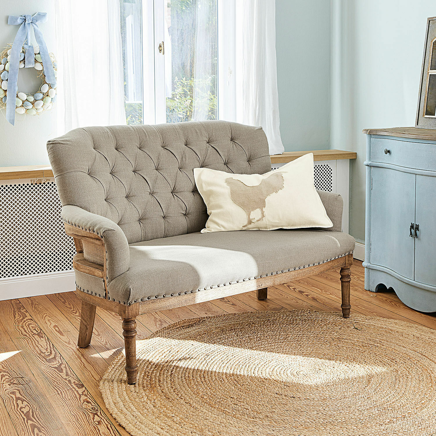 Sofa Kingsley Beżowa tapicerowana sofa z drewnianą ramą i ozdobnymi guzikami w jasnym salonie