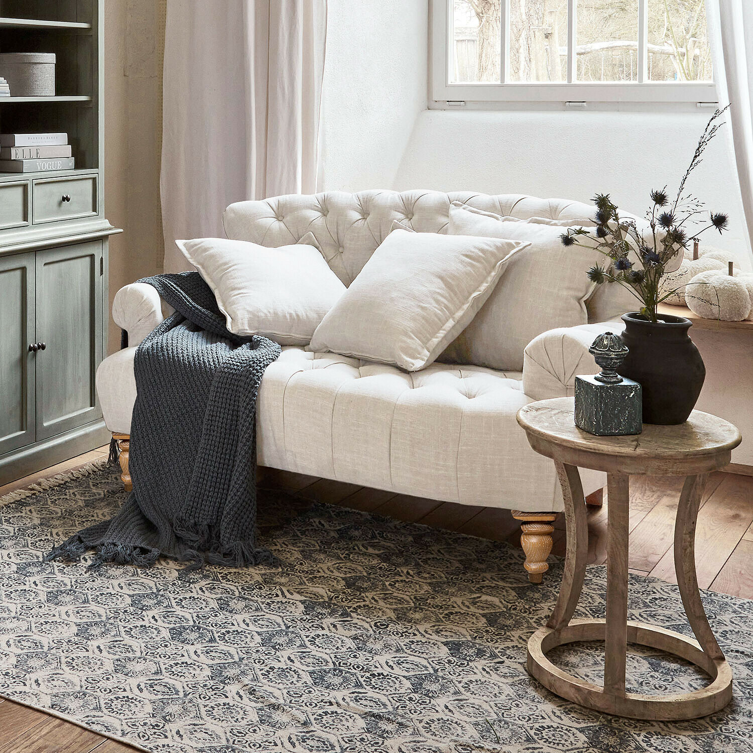 Sofa Springfield Village Beżowa pikowana sofa z lnu z poduszkami i szarym dzianym kocem w przytulnym salonie z drewnianym stolikiem