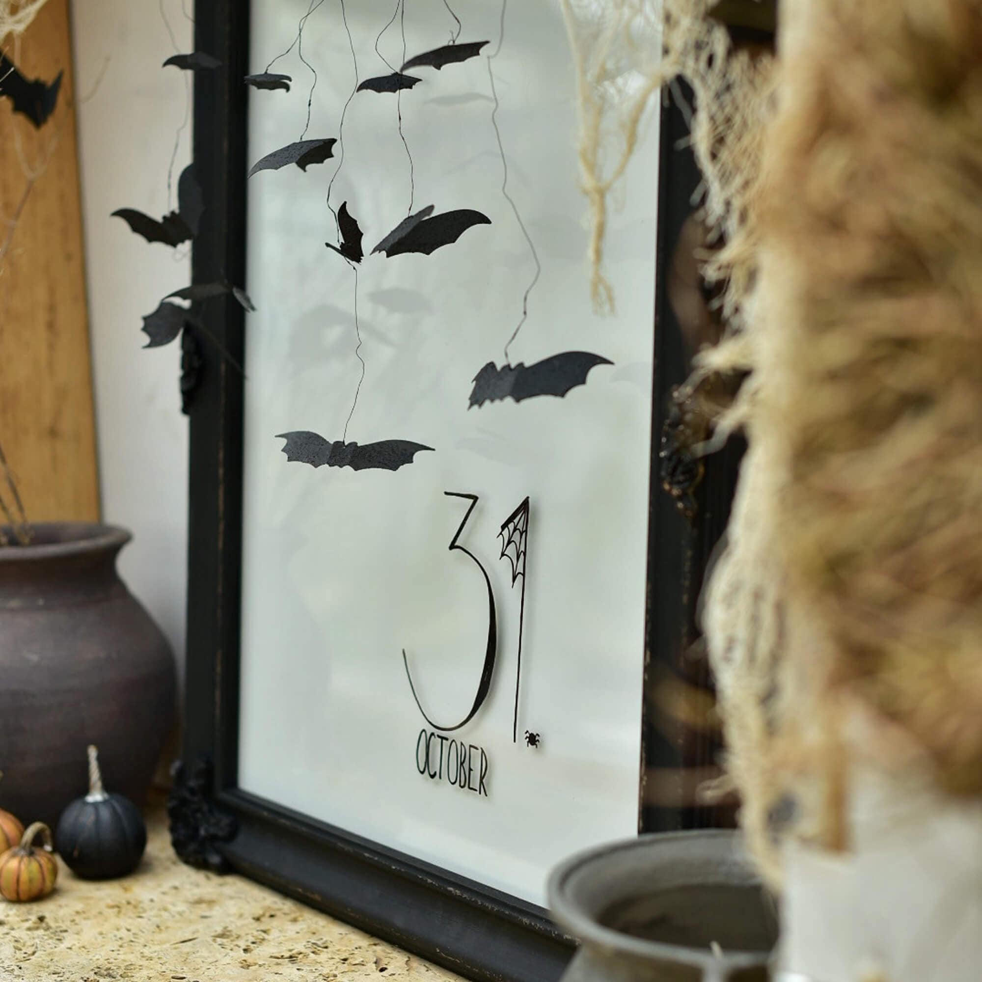 Dekoracja na Halloween z czarnymi papierowymi nietoperzami i napisem 31 października w ramce