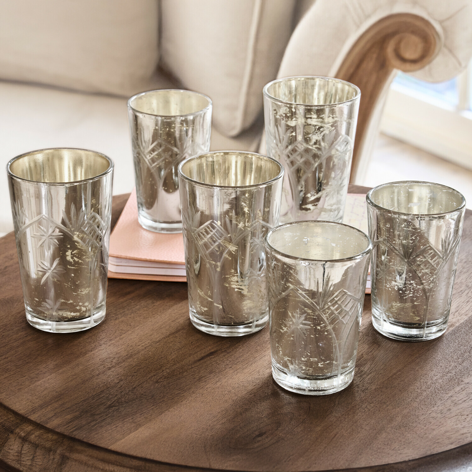 Zestaw sześciu szklanych świeczników z grawerowanym wzorem i srebrnym wykończeniem na drewnianym stole