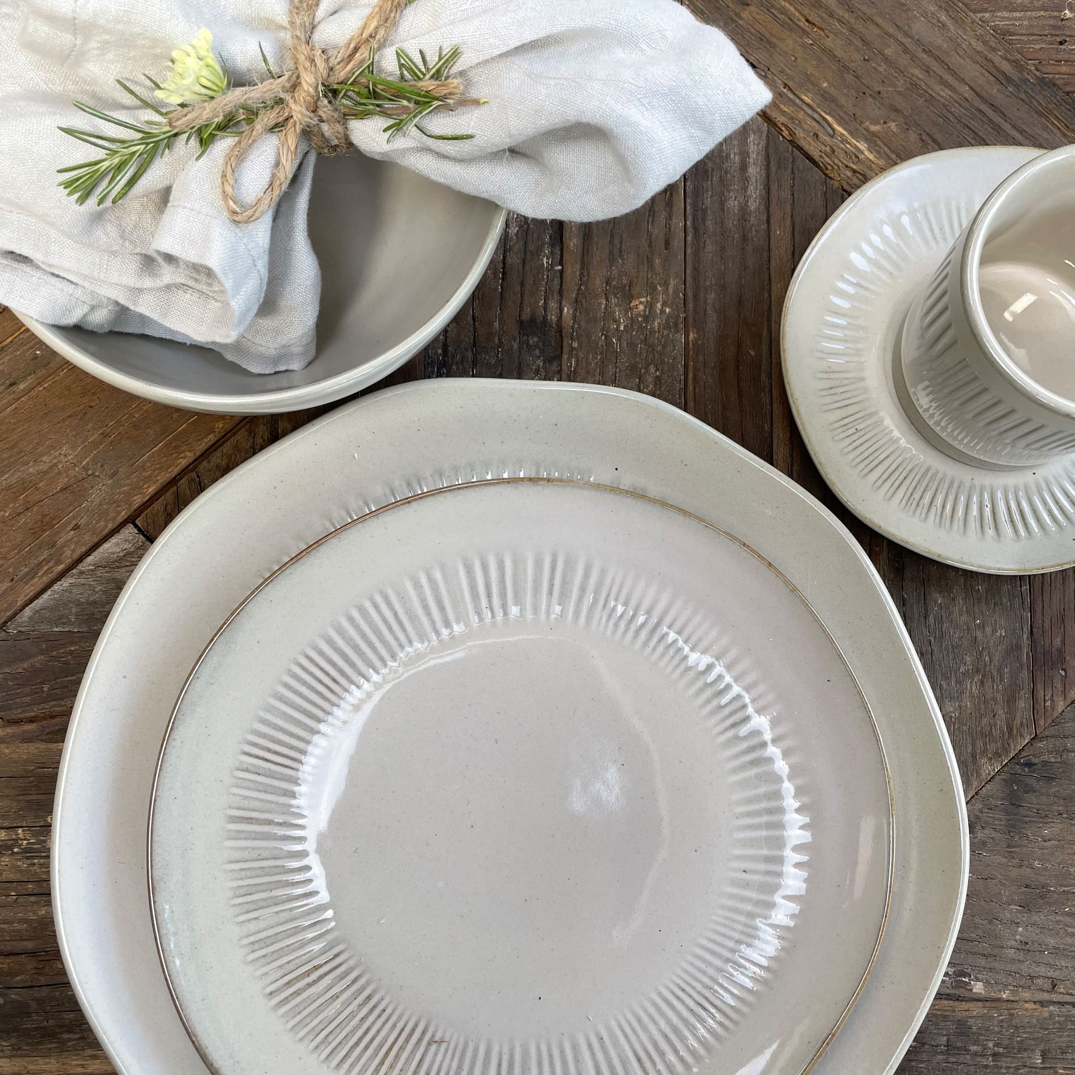 Zestaw kremowej ceramiki stołowej na drewnianym stole z lnianą serwetką i gałązką rozmarynu