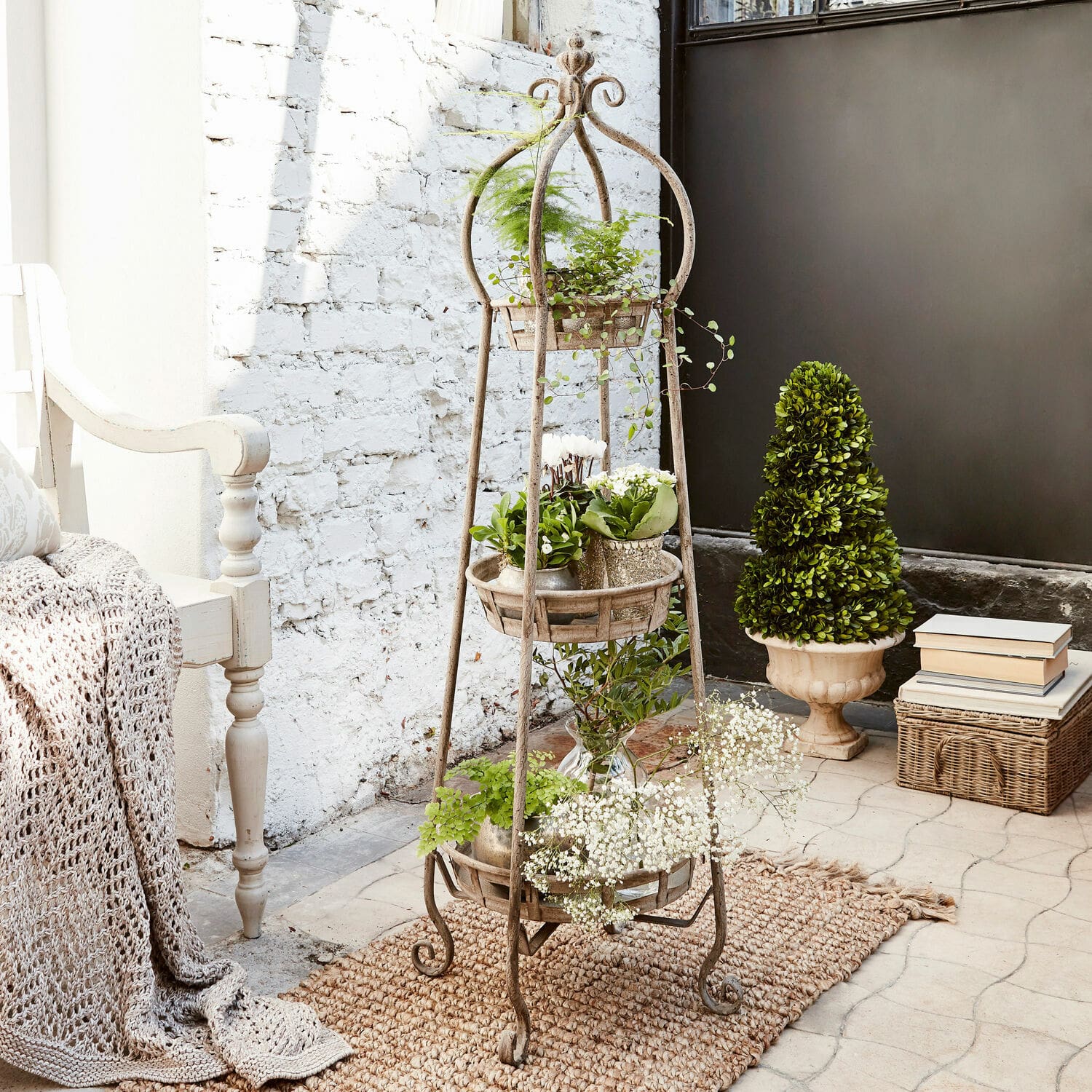 Metalowa, rustykalna stojąca donica z trzema poziomami na rośliny w jasnym wnętrzu z naturalnym dywanem