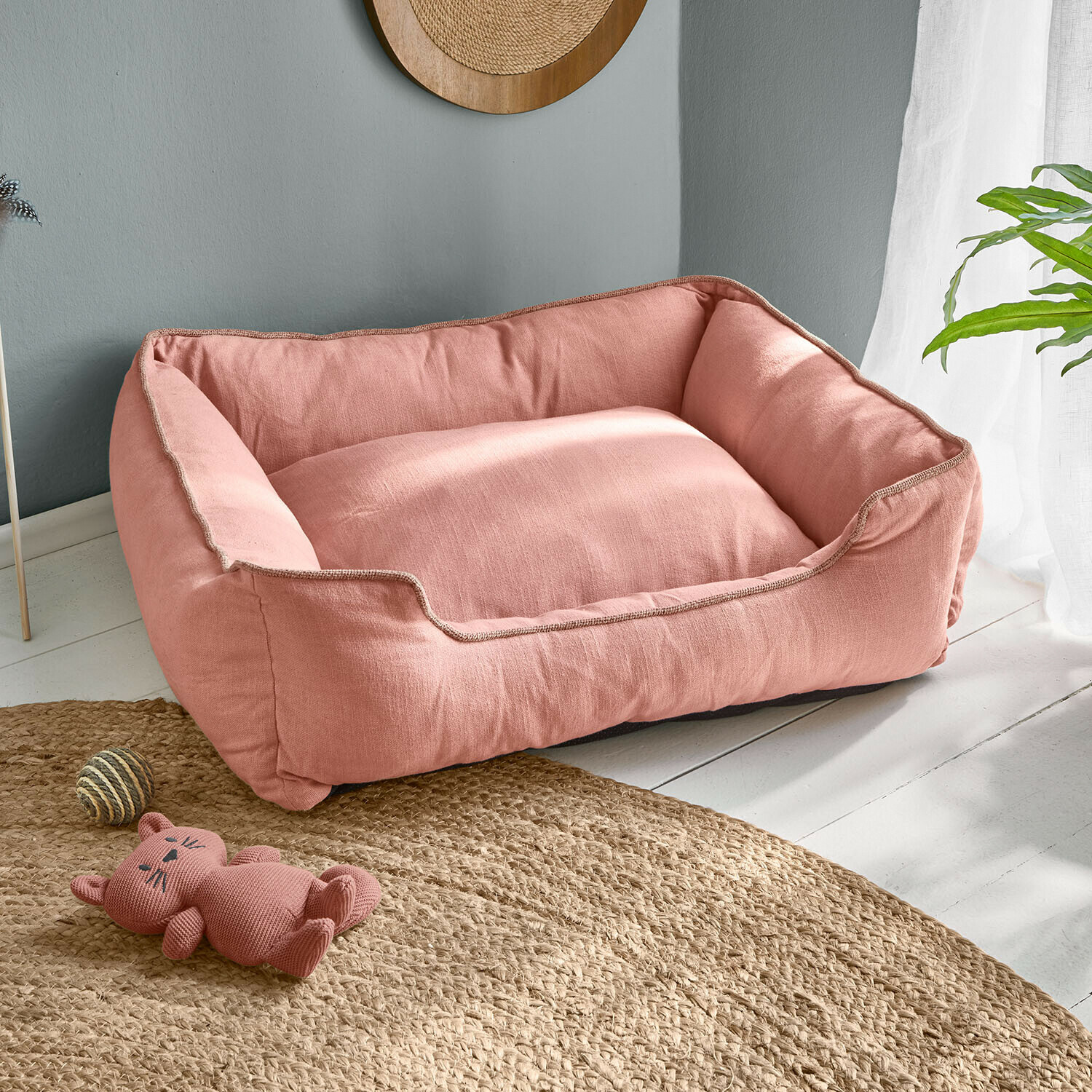 Różowe legowisko dla psa z miękkiego materiału na jasnej podłodze z zabawką kota i piłką