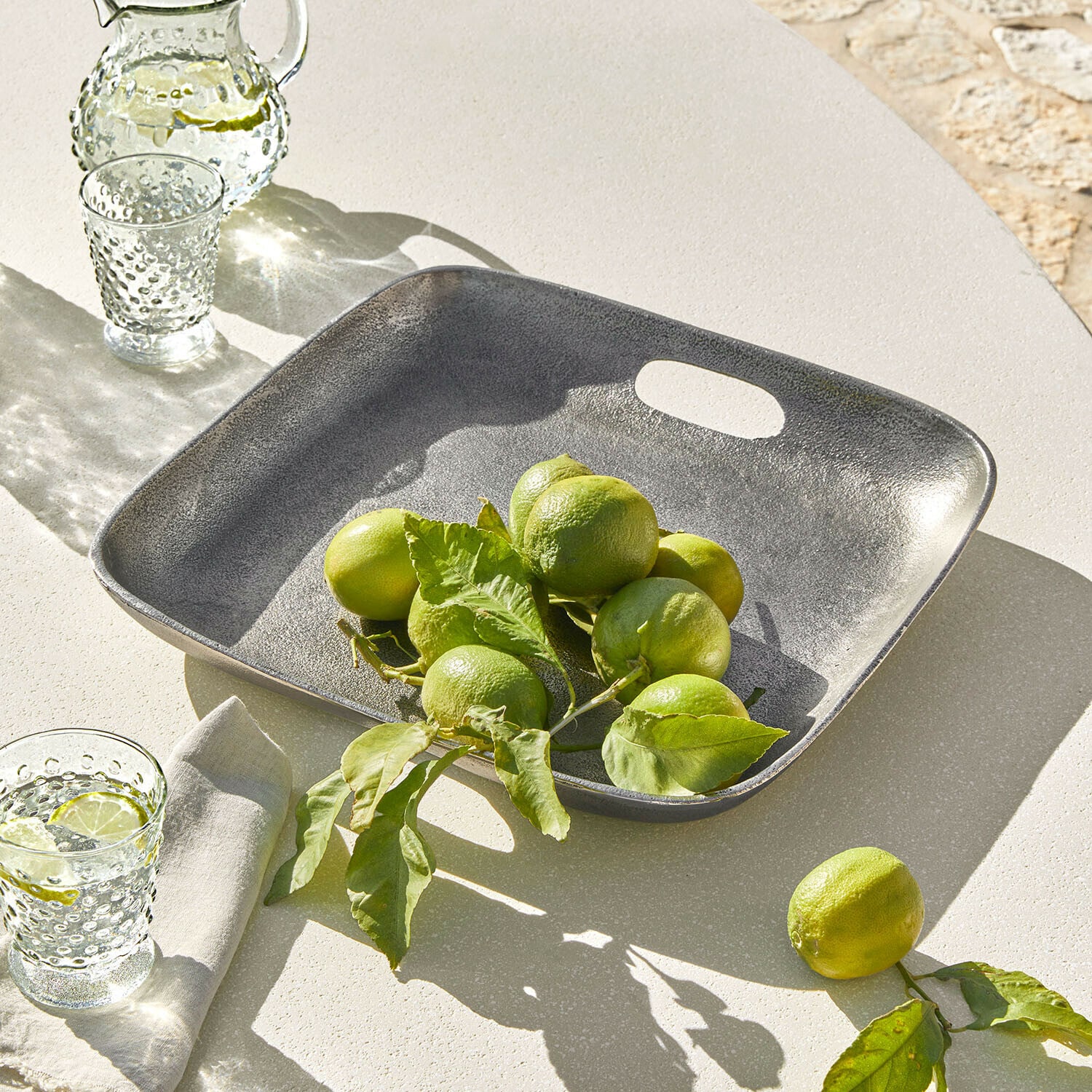 Kwadratowa taca z metalu w kolorze szarym z zielonymi limonkami na jasnym stole, dekoracja stołu