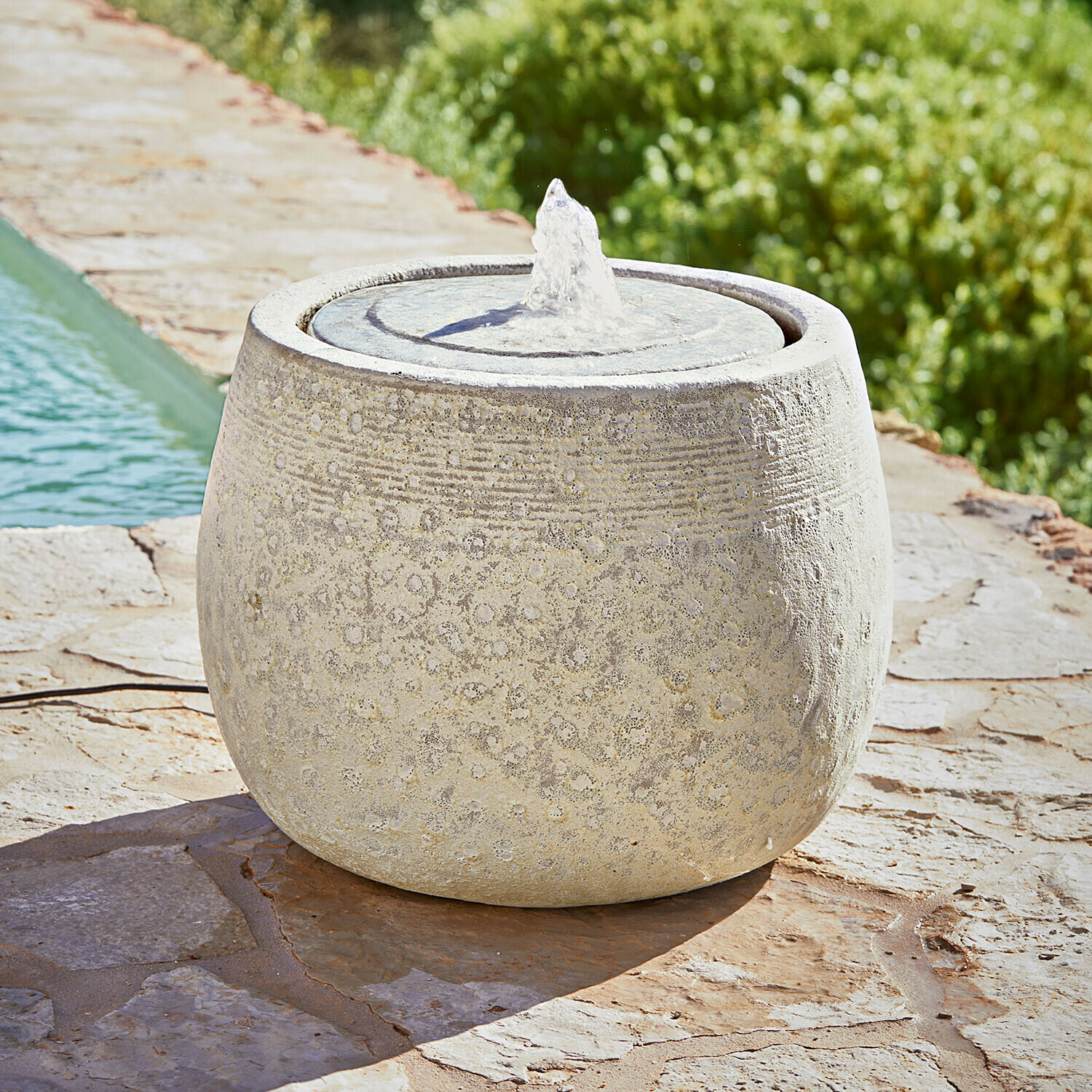 Okrągła fontanna ogrodowa z jasnego kamienia z delikatnym wzorem i strumieniem wody na tarasie