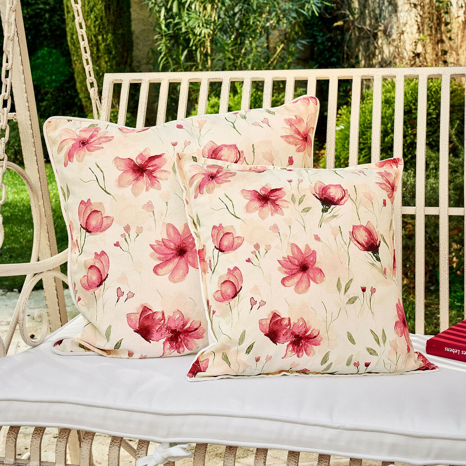 Dwa kwiatowe poduszki dekoracyjne na białej huśtawce ogrodowej, materiał bawełna, jasnoróżowe wzory