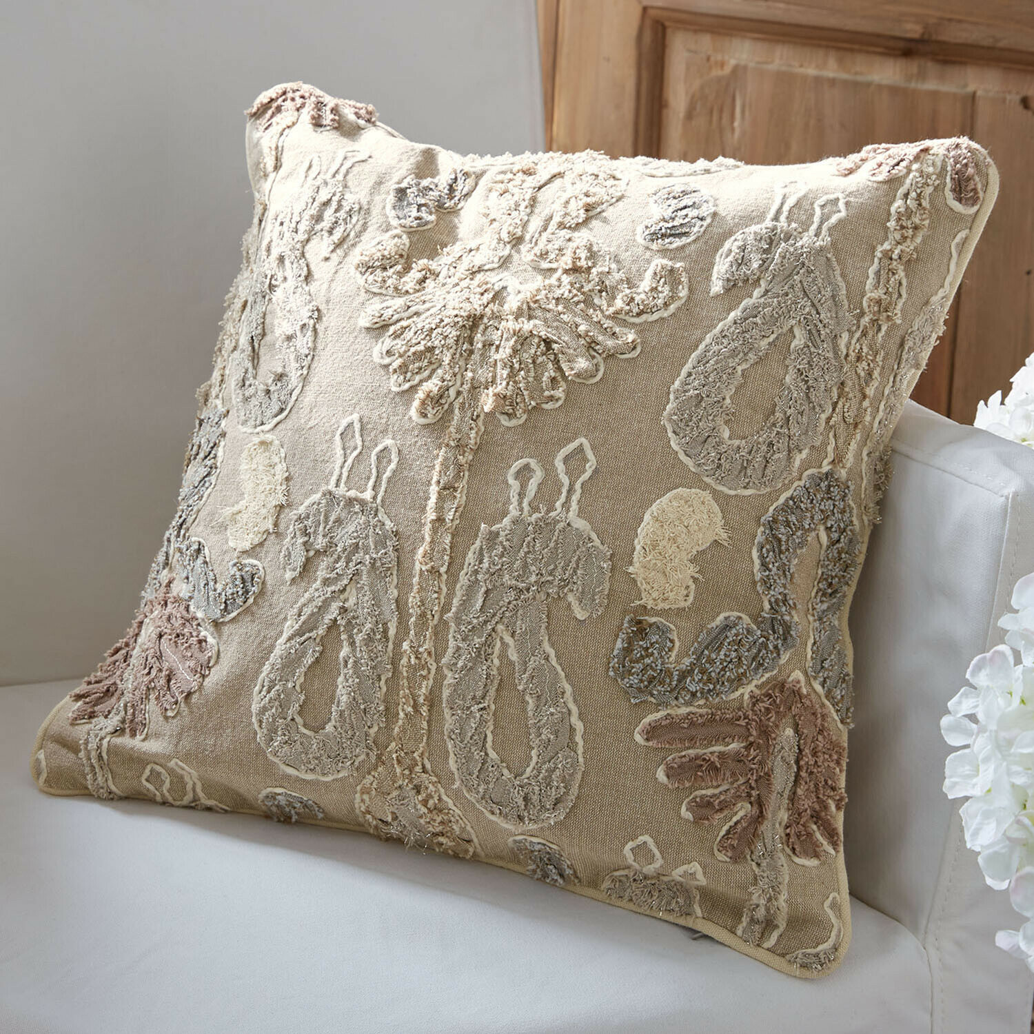 Beżowa dekoracyjna poduszka z haftowanym wzorem w naturalnych kolorach na kanapie