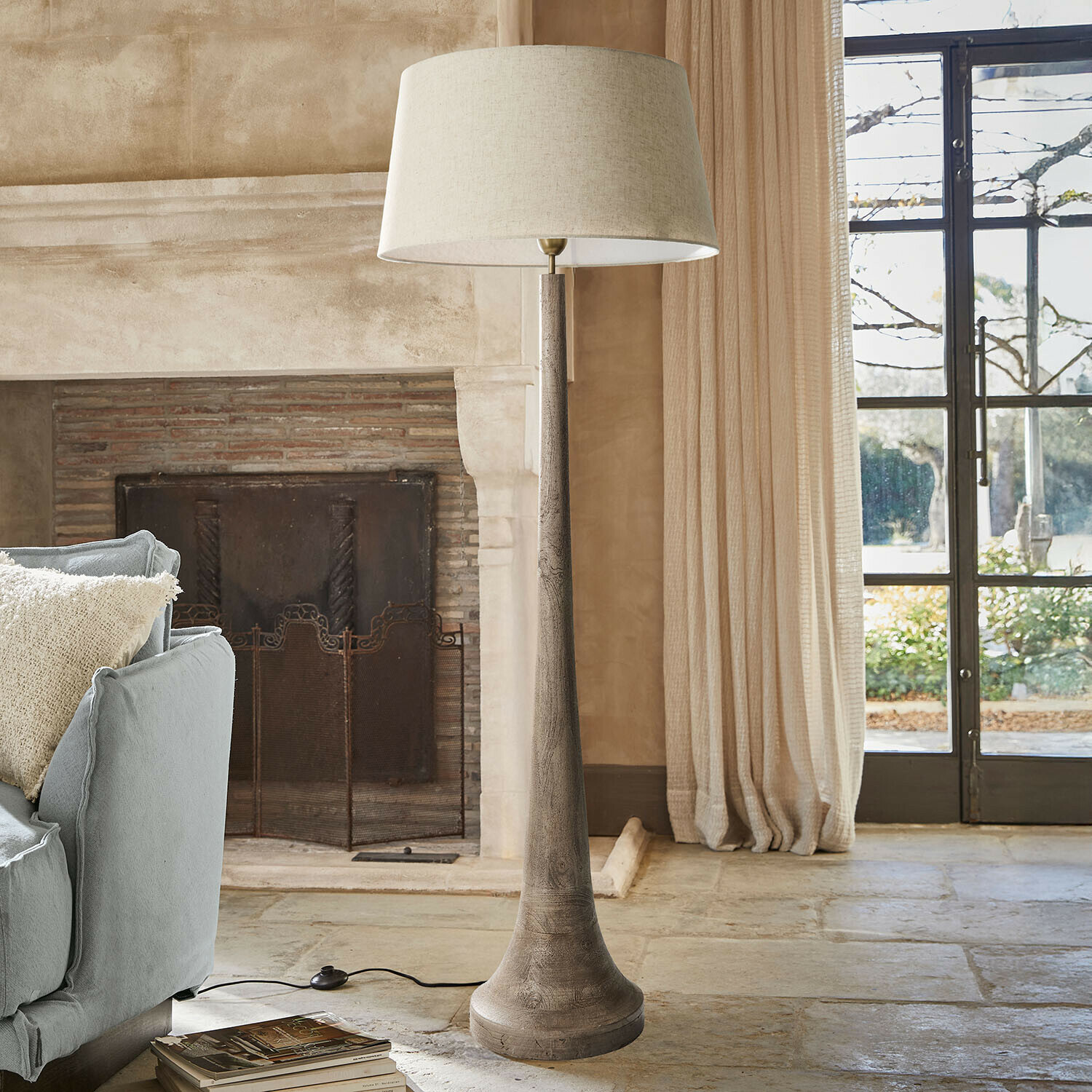 Stojąca lampa podłogowa z drewnianą podstawą i beżowym abażurem w przytulnym salonie z kominkiem