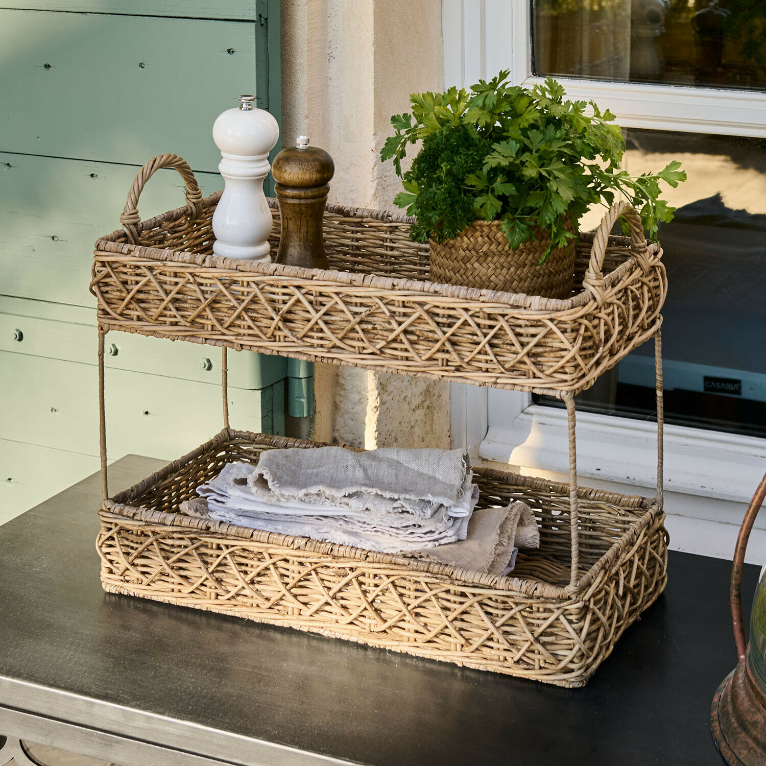 Dwupoziomowy kosz z rattanu w naturalnym kolorze z przyprawami i zielonymi ziołami na stole