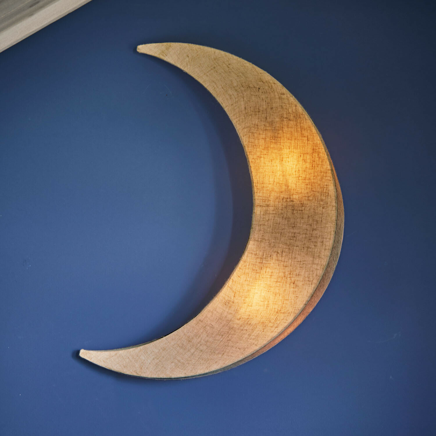 Lampa ścienna Jollymoon Lampka ścienna w kształcie księżyca z materiału w beżowym kolorze na niebieskiej ścianie