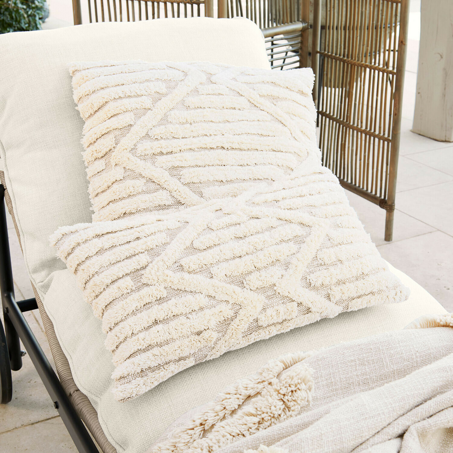 Dwa kremowe poduszki dekoracyjne z miękkiego materiału o geometrycznym wzorze na jasnym leżaku