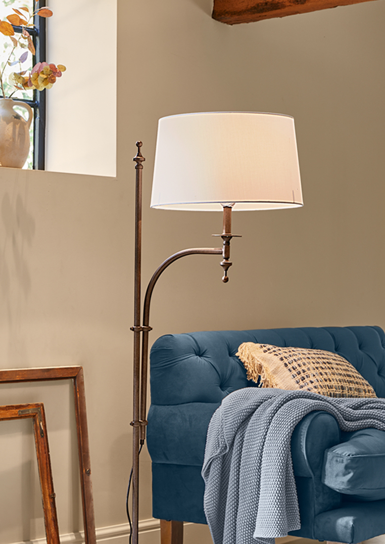 Stojąca lampa podłogowa z metalową ramą i białym abażurem obok niebieskiej sofy z kocem