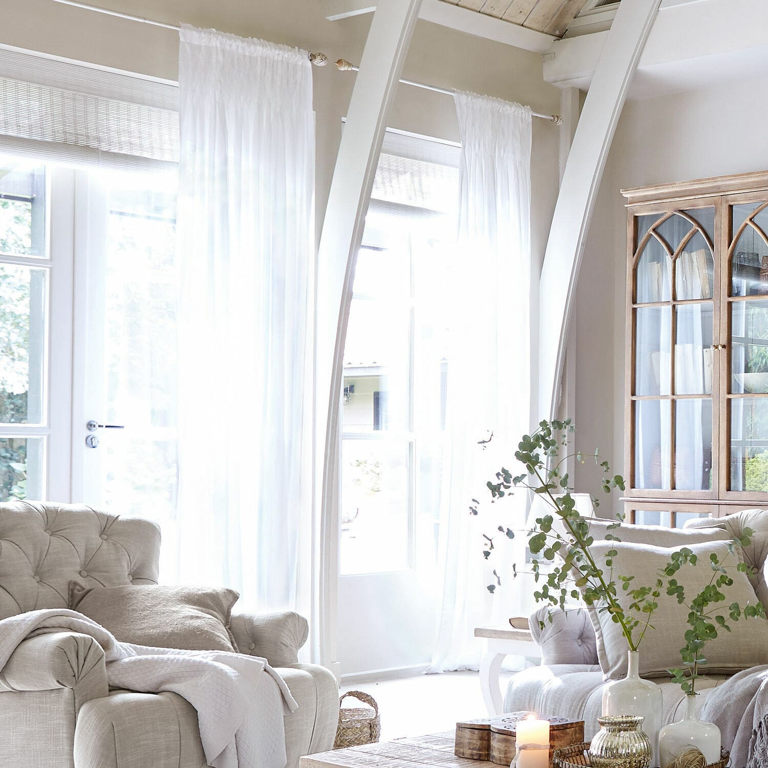 Firana Otilie Jasny salon z beżową tapicerką, białymi zasłonami i drewnianą witryną w stylu vintage