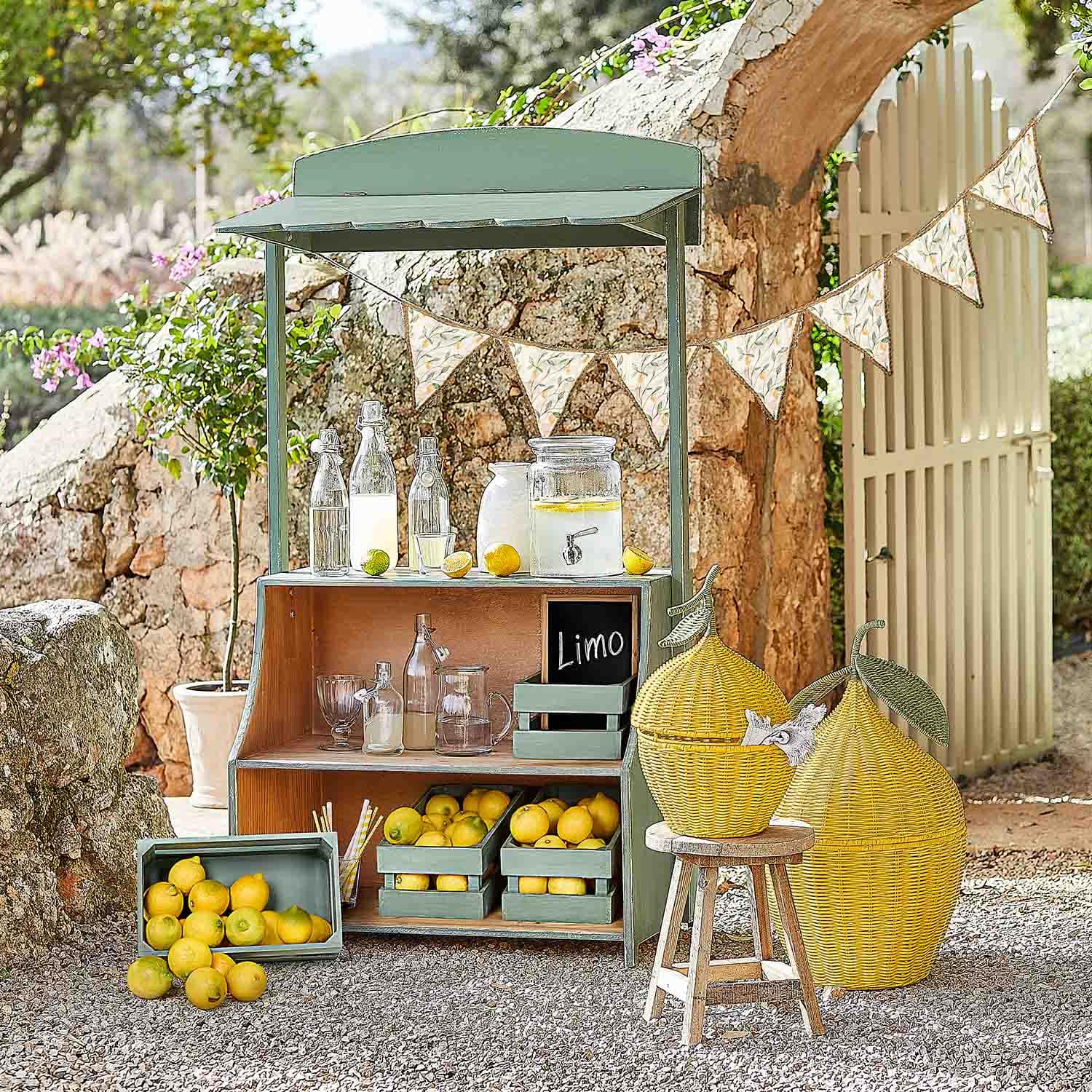 Zielony drewniany stojak z cytrynami i szklanymi butelkami na lemoniadę w ogrodzie