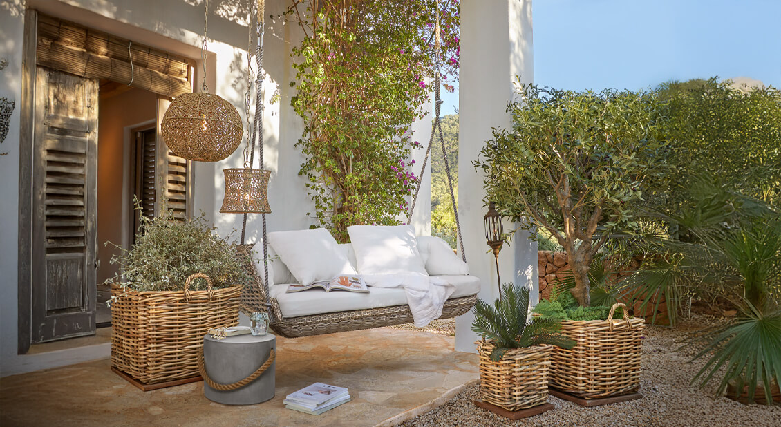 Huśtawka z wikliny z białymi poduszkami na tarasie z lampami z rattanu i roślinami w wiklinowych koszach