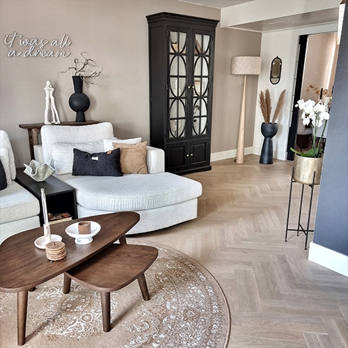 Przytulny salon z jasnoszarym narożnikiem, czarną witryną i drewnianym stolikiem kawowym na okrągłym dywanie