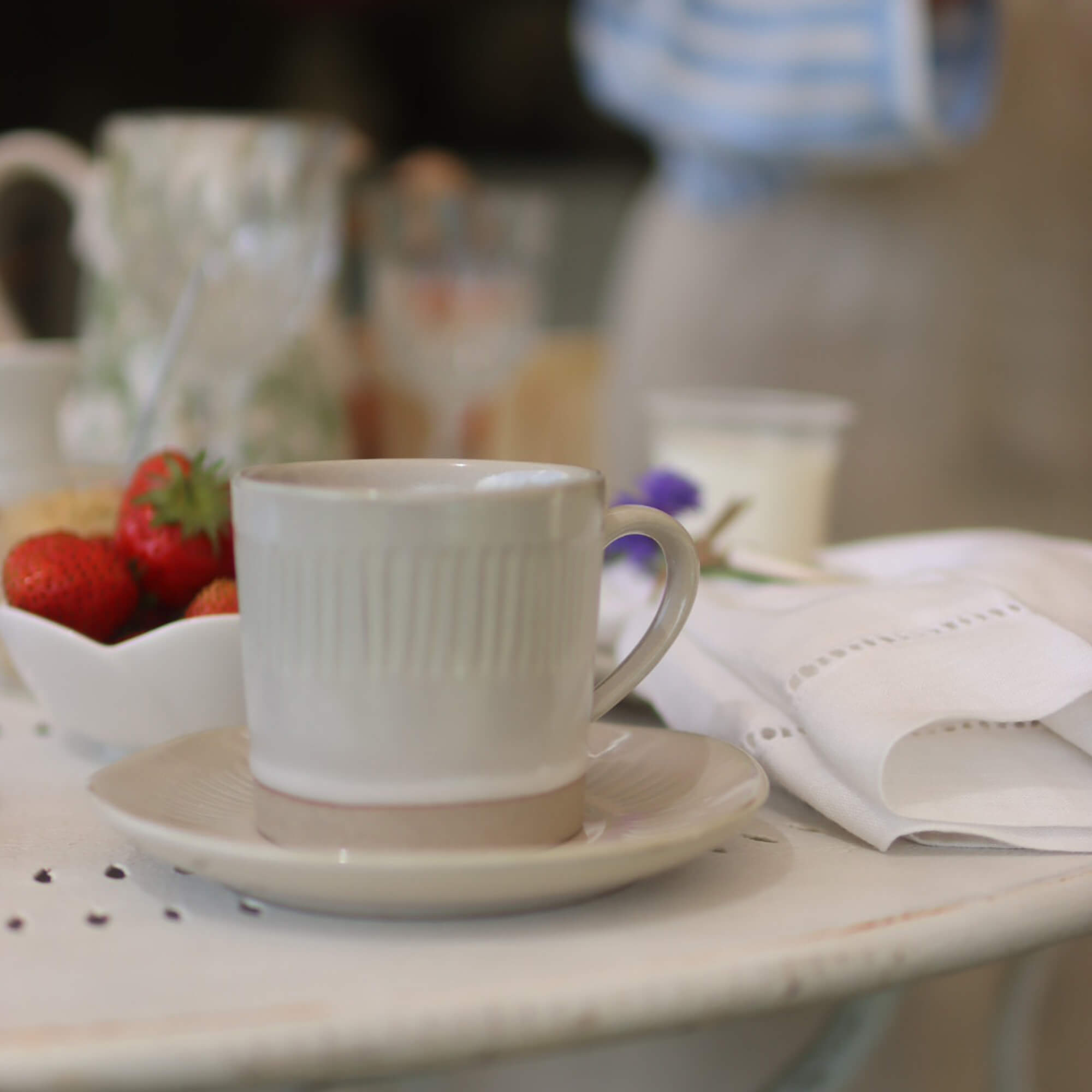 Beżowa ceramiczna filiżanka z talerzykiem na białym stole z truskawkami i lnianą serwetką