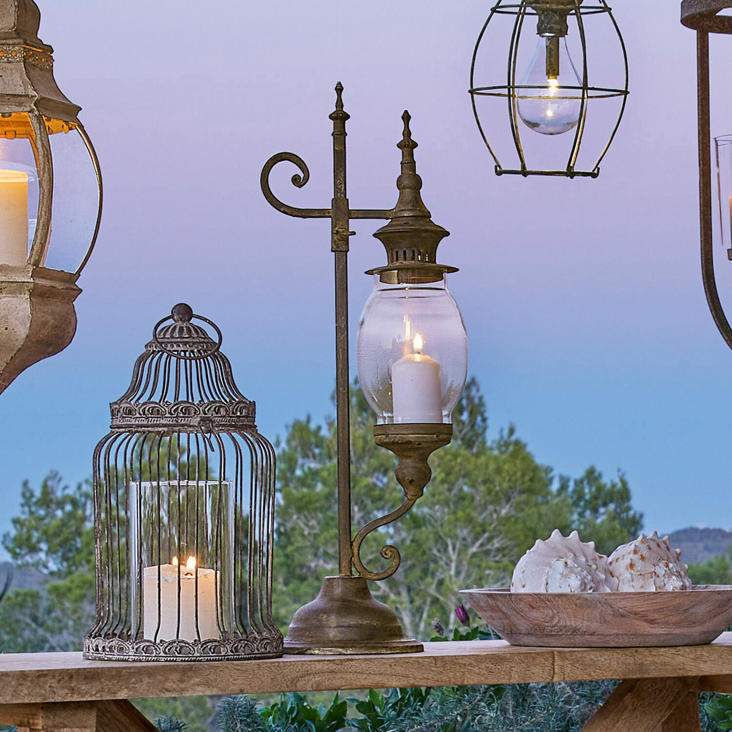 Lampion Bowral Metalowa latarnia z przezroczystym szkłem i świecą na drewnianym stole na zewnątrz z dekoracją muszli
