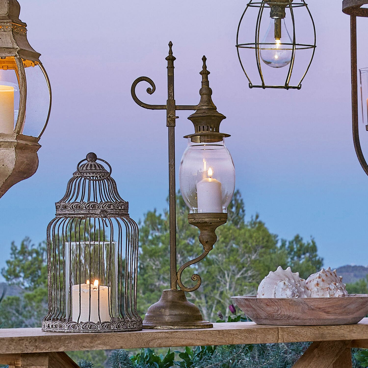 Lampion Bowral Metalowa latarnia z przezroczystym szkłem i świecą na drewnianym stole na zewnątrz z dekoracją muszli
