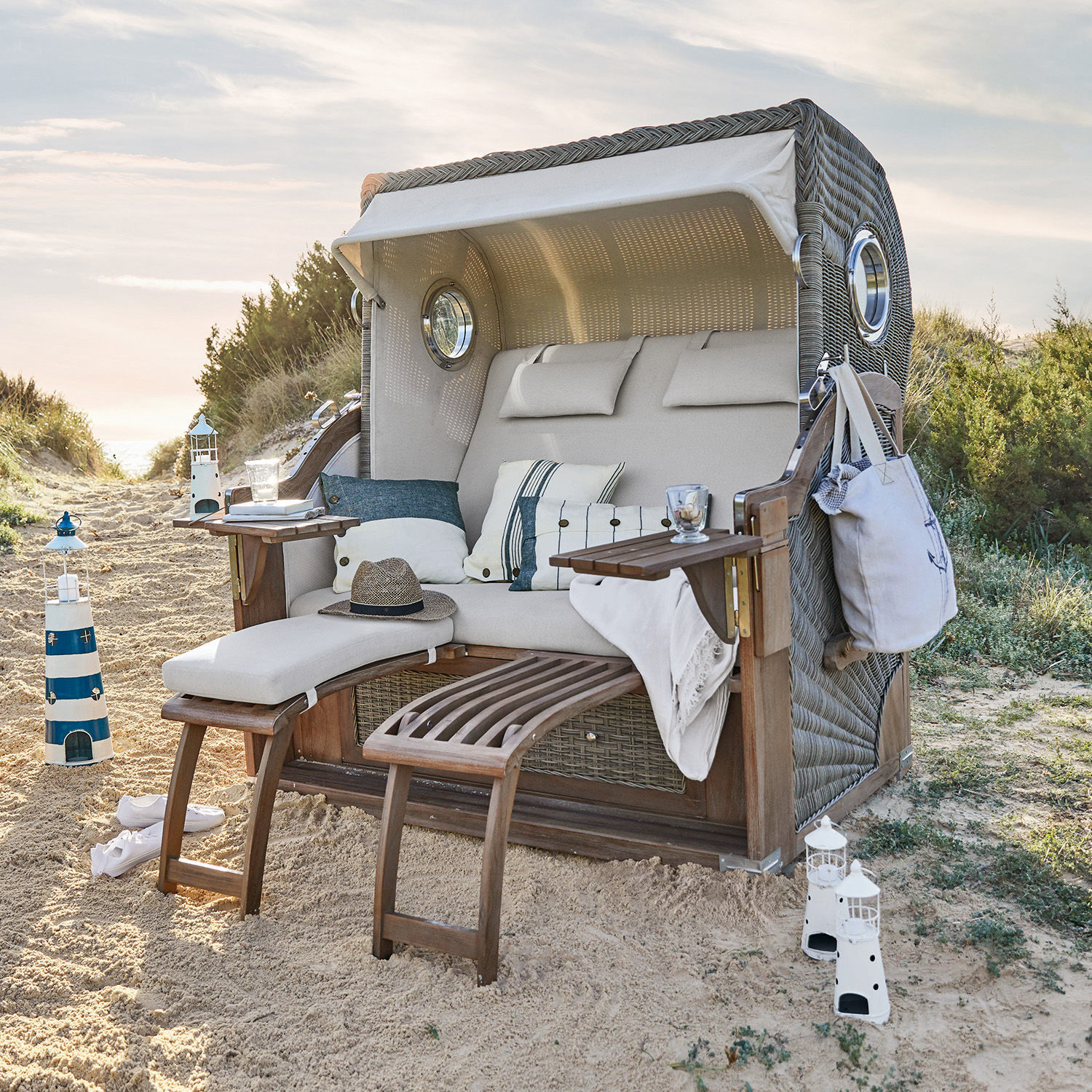 Kosz plażowy Clifford Beach Wiklinowy fotel plażowy z beżową poduszką i drewnianymi podnóżkami na piasku, meble ogrodowe