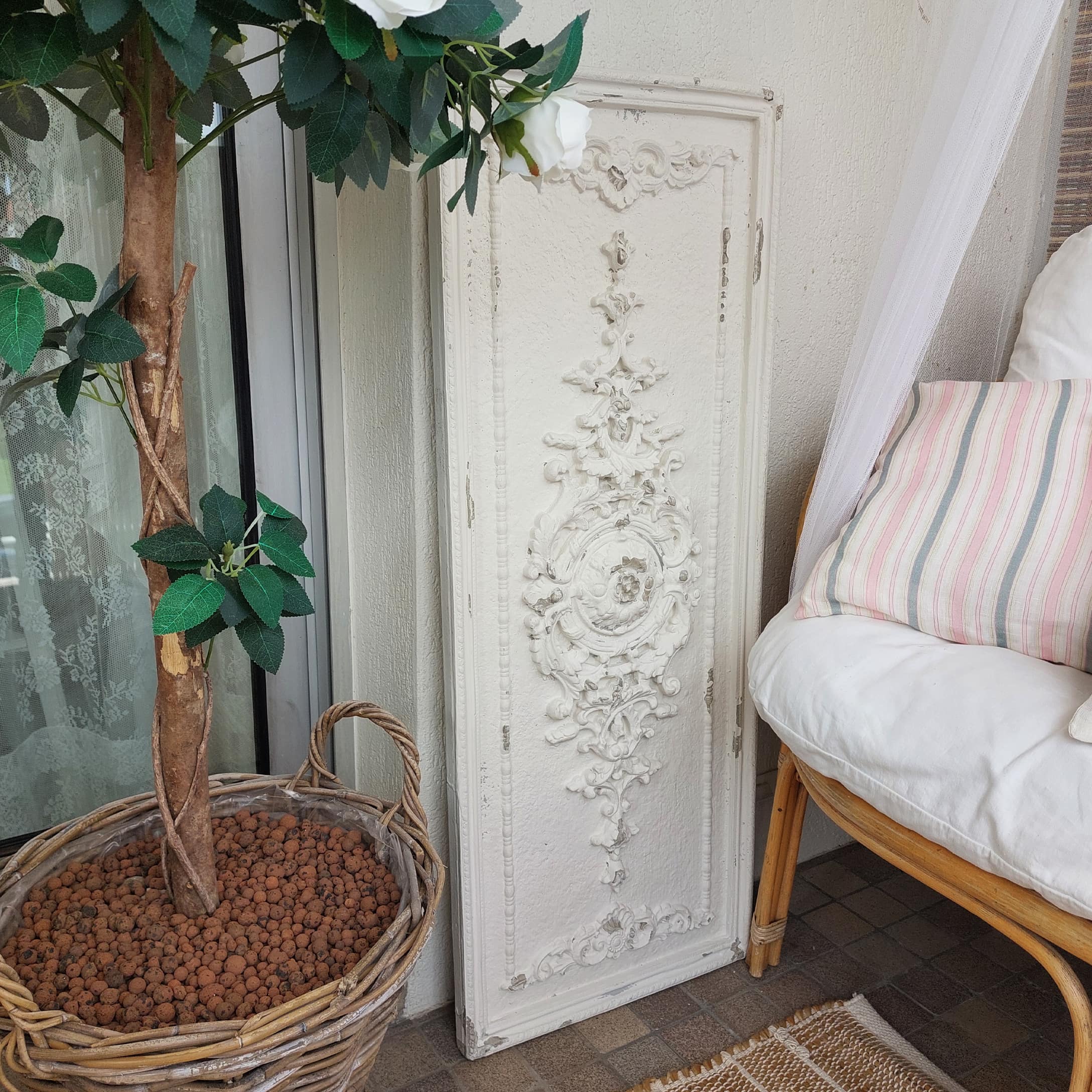 Biały dekoracyjny panel ścienny z ornamentem w stylu vintage obok wiklinowego kosza z rośliną