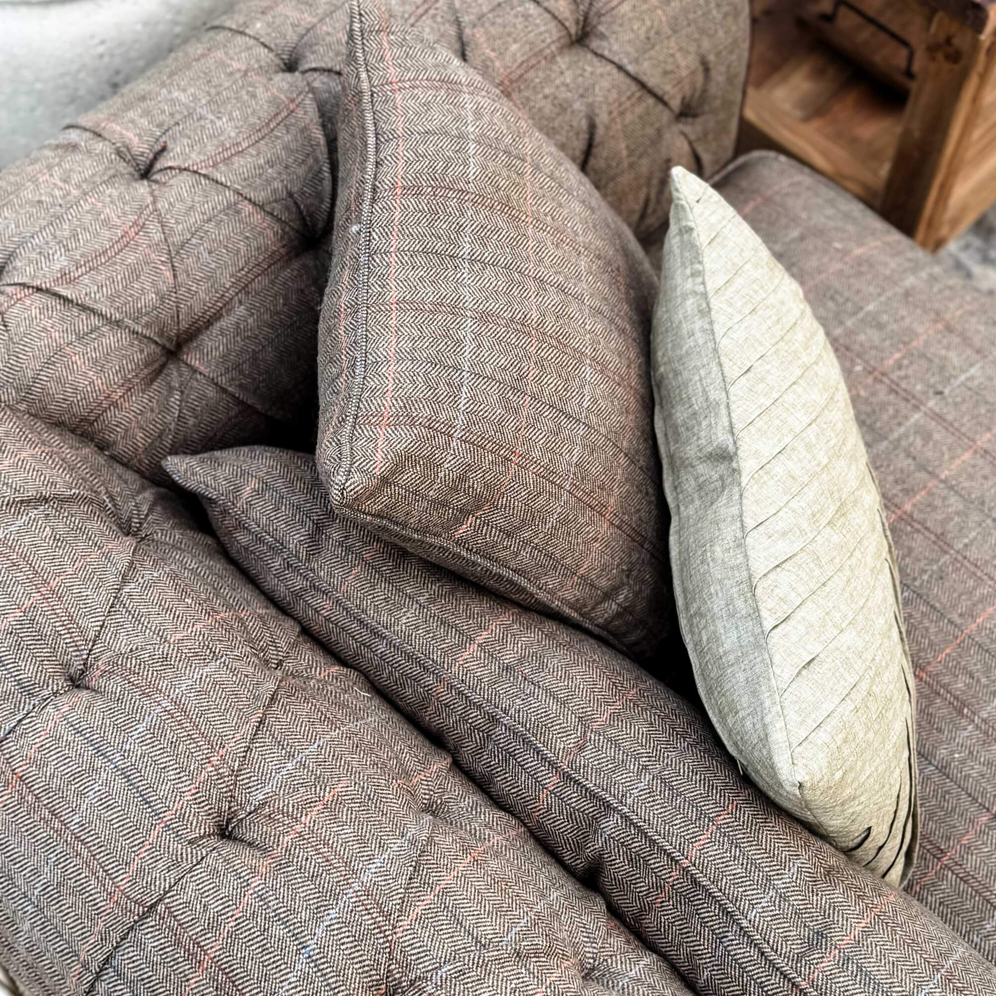 Brązowa tapicerowana sofa z poduszkami w jodełkę i jasną dekoracyjną poduszką do salonu